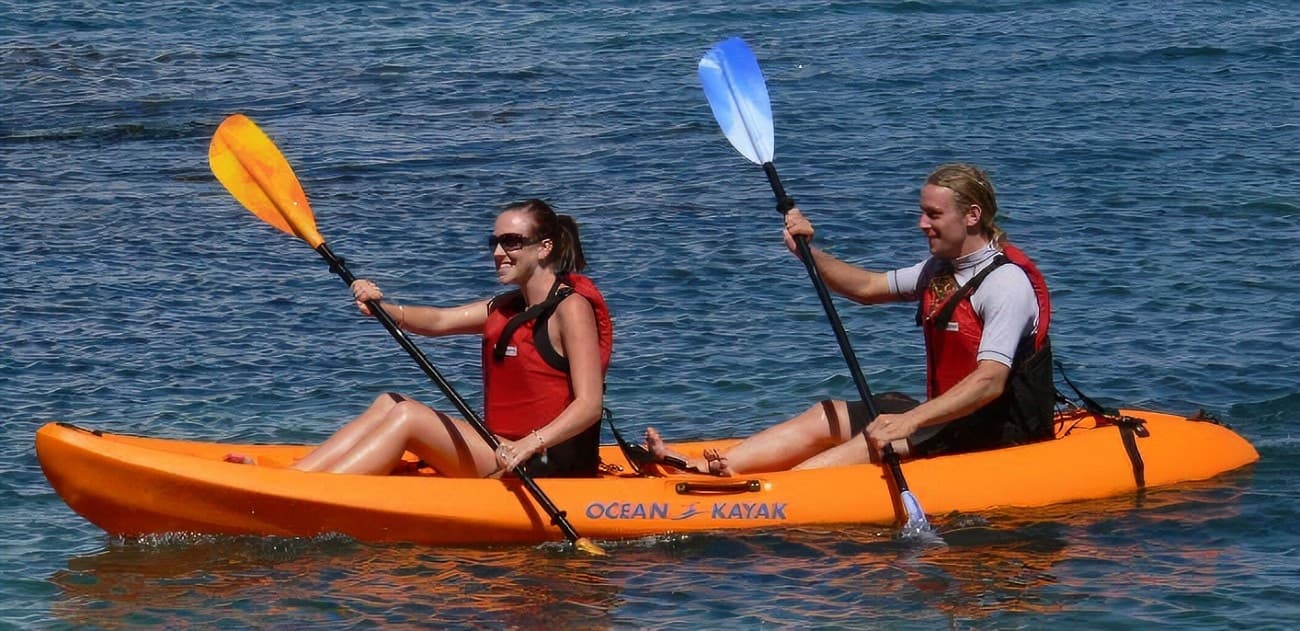 Two kayakers tandem paddling on open ocean water, sunny