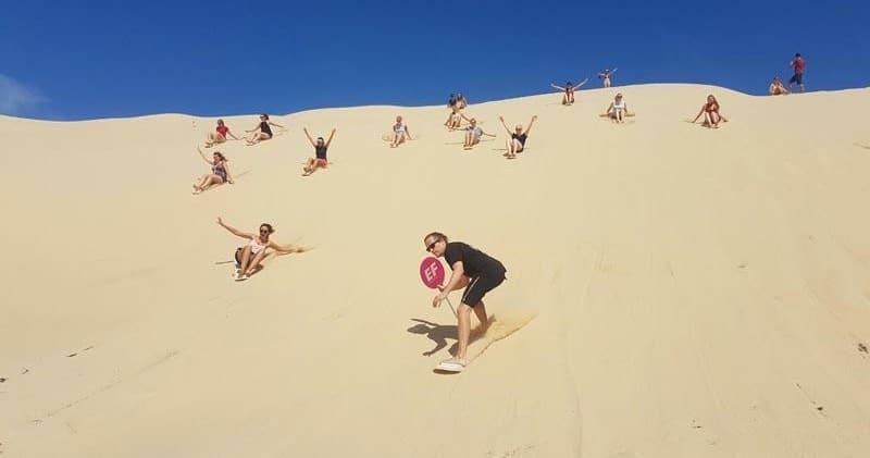 Sandboarders sliding down expansive golden sand dunes