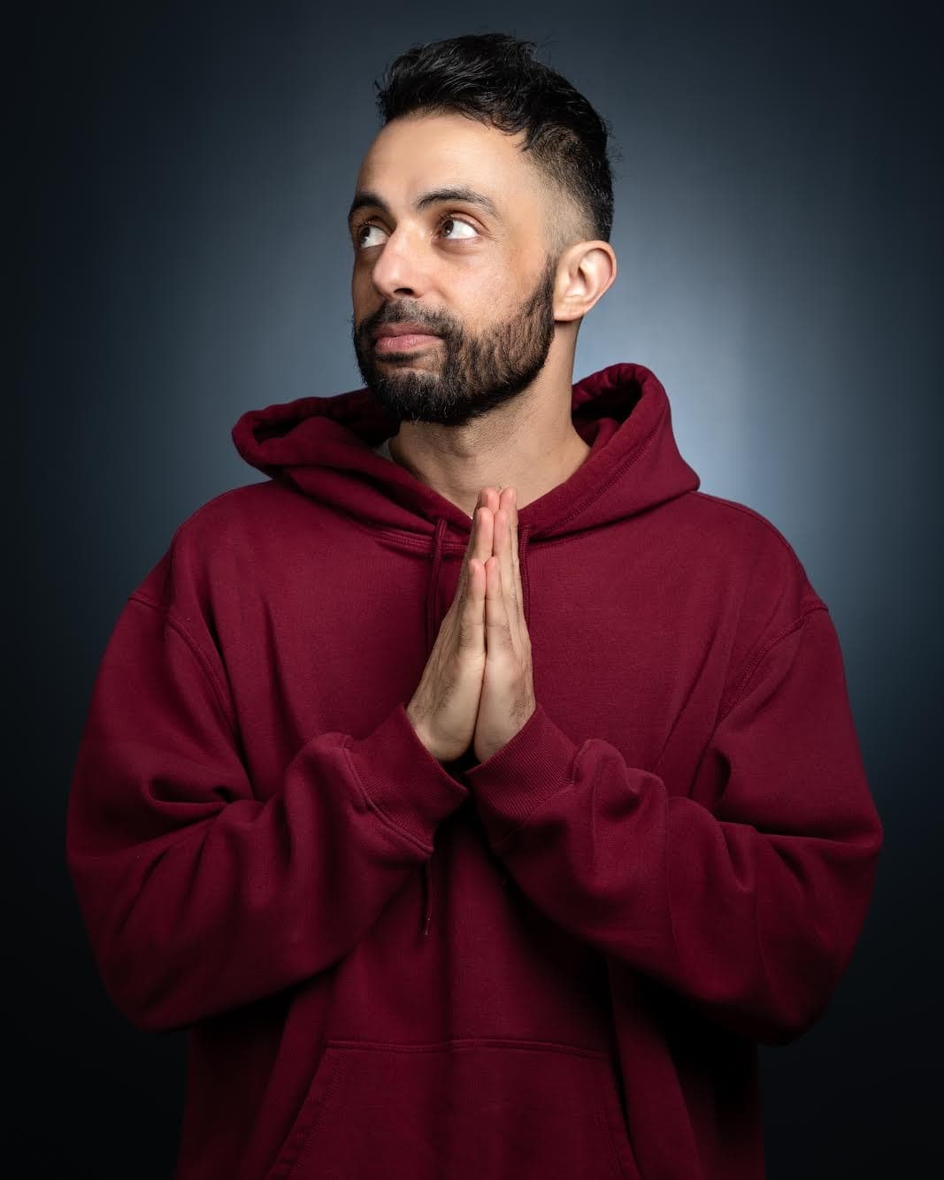 Man in maroon hoodie posed in studio with thoughtful gaze
