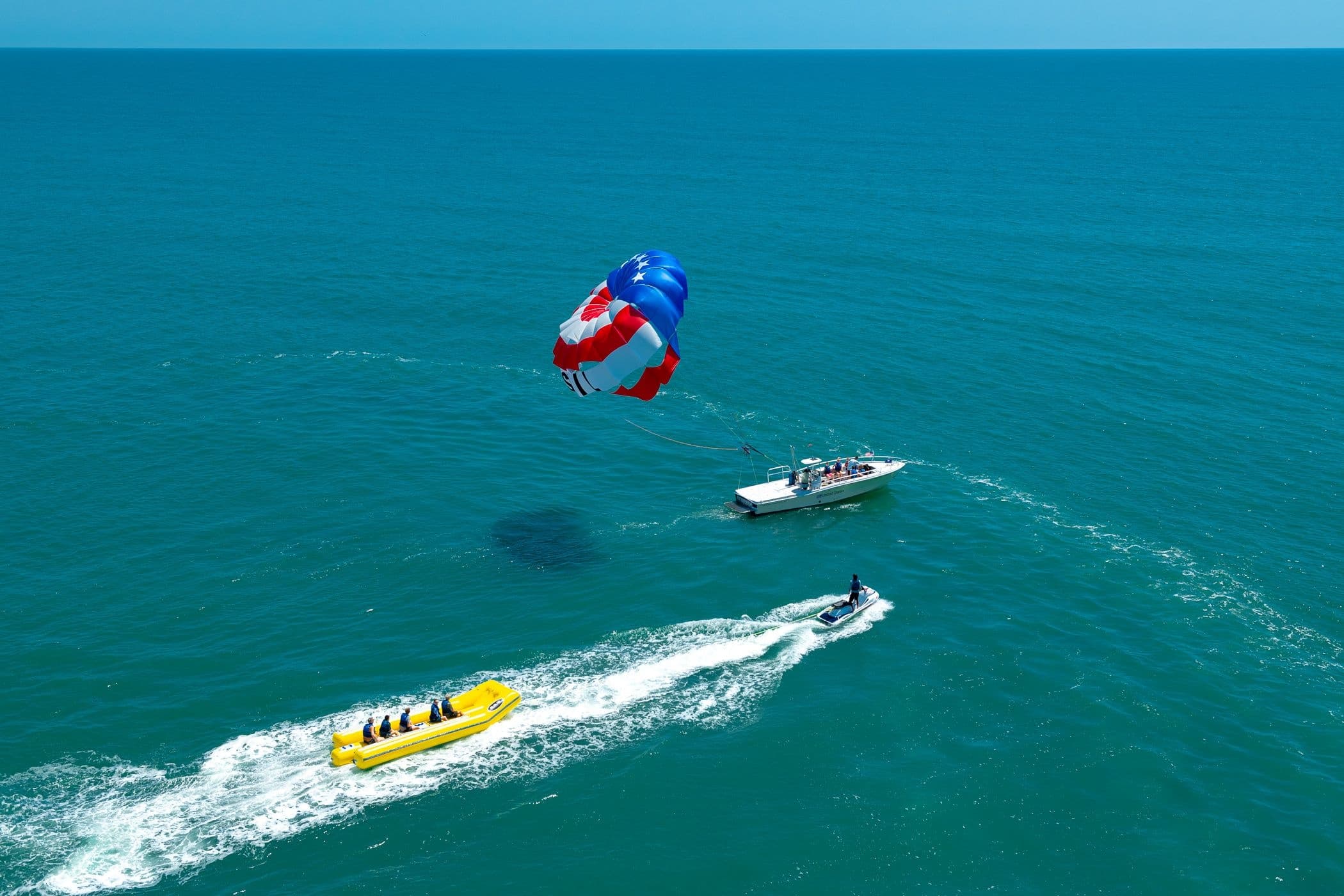Aerial view of parasail and tow boat over open turquoise sea