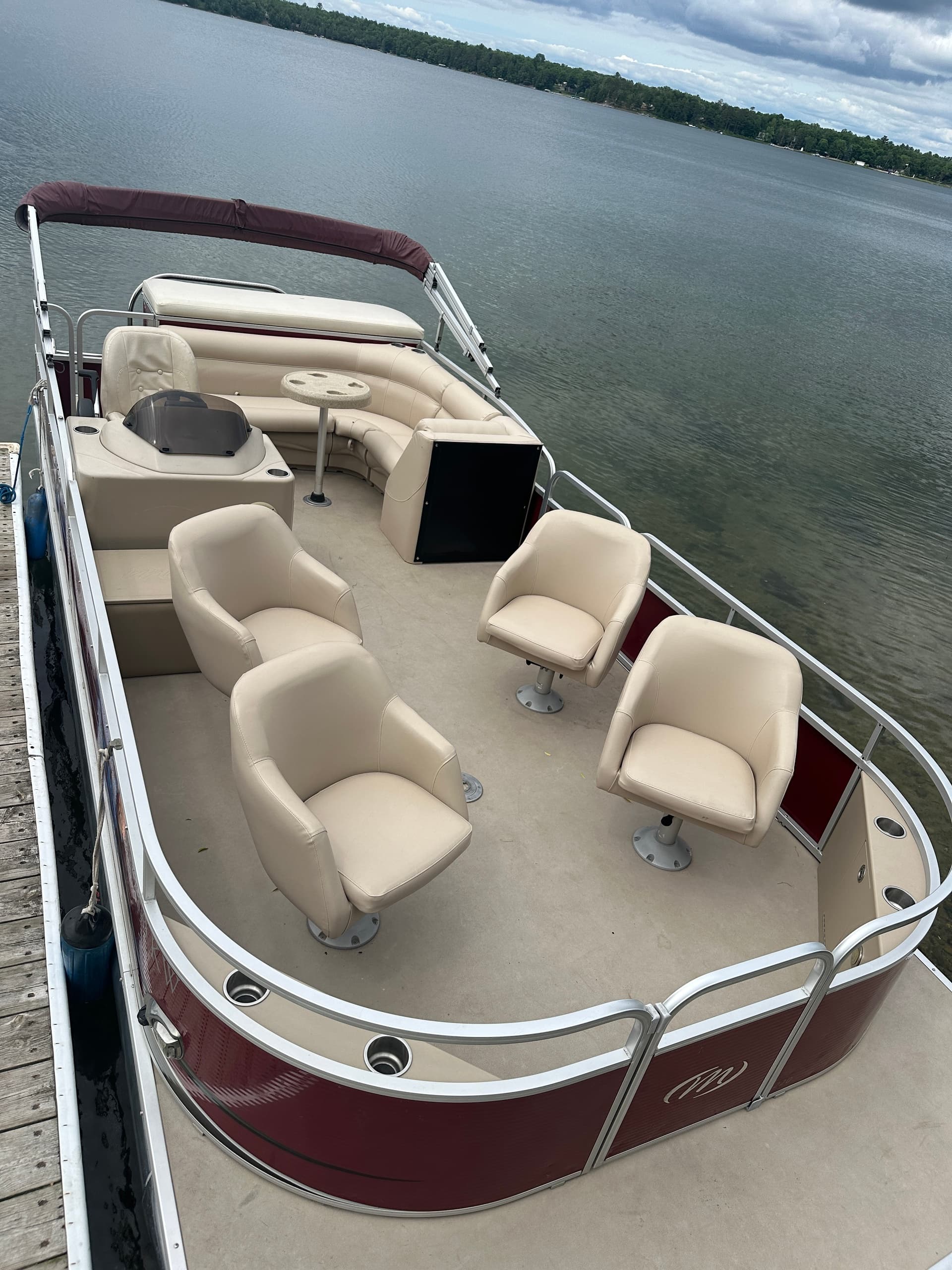 Bow seating pontoon with maroon accents on calm summer lake
