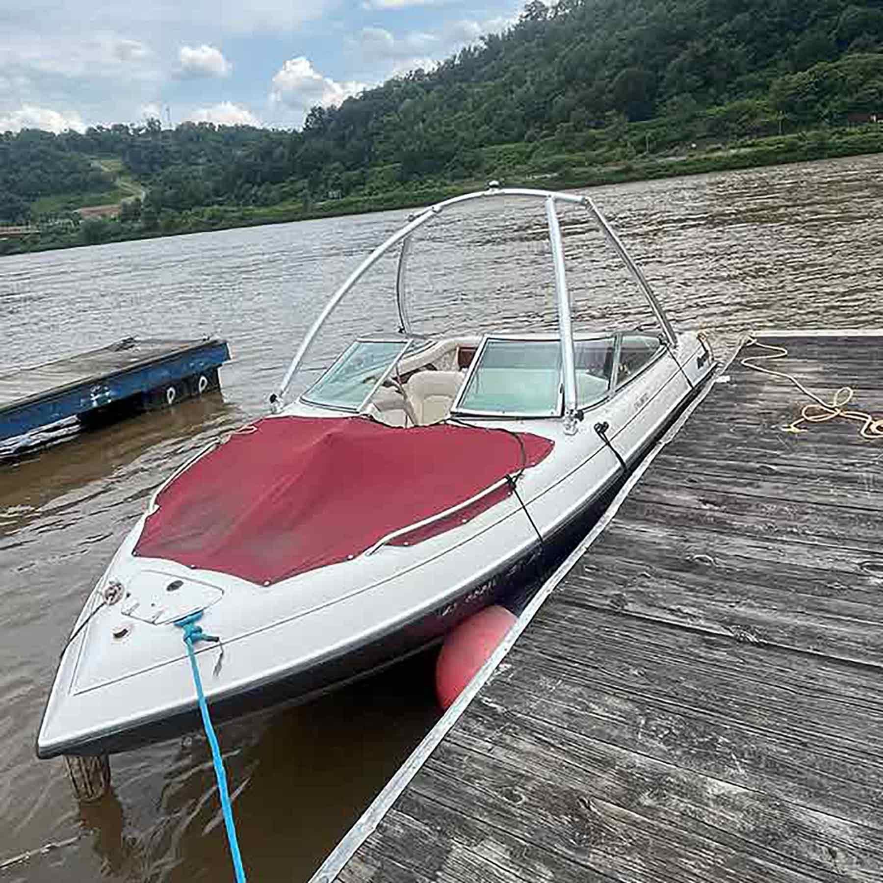 Bow of speedboat docked on river with forested shoreline backdrop