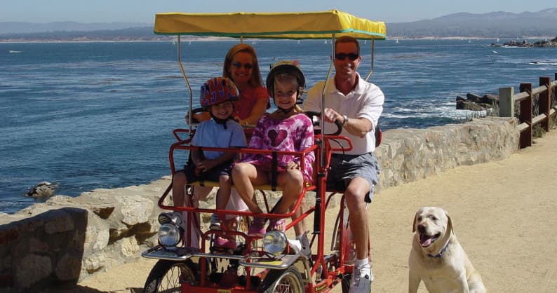 Family surrey ride along ocean promenade with dog nearby