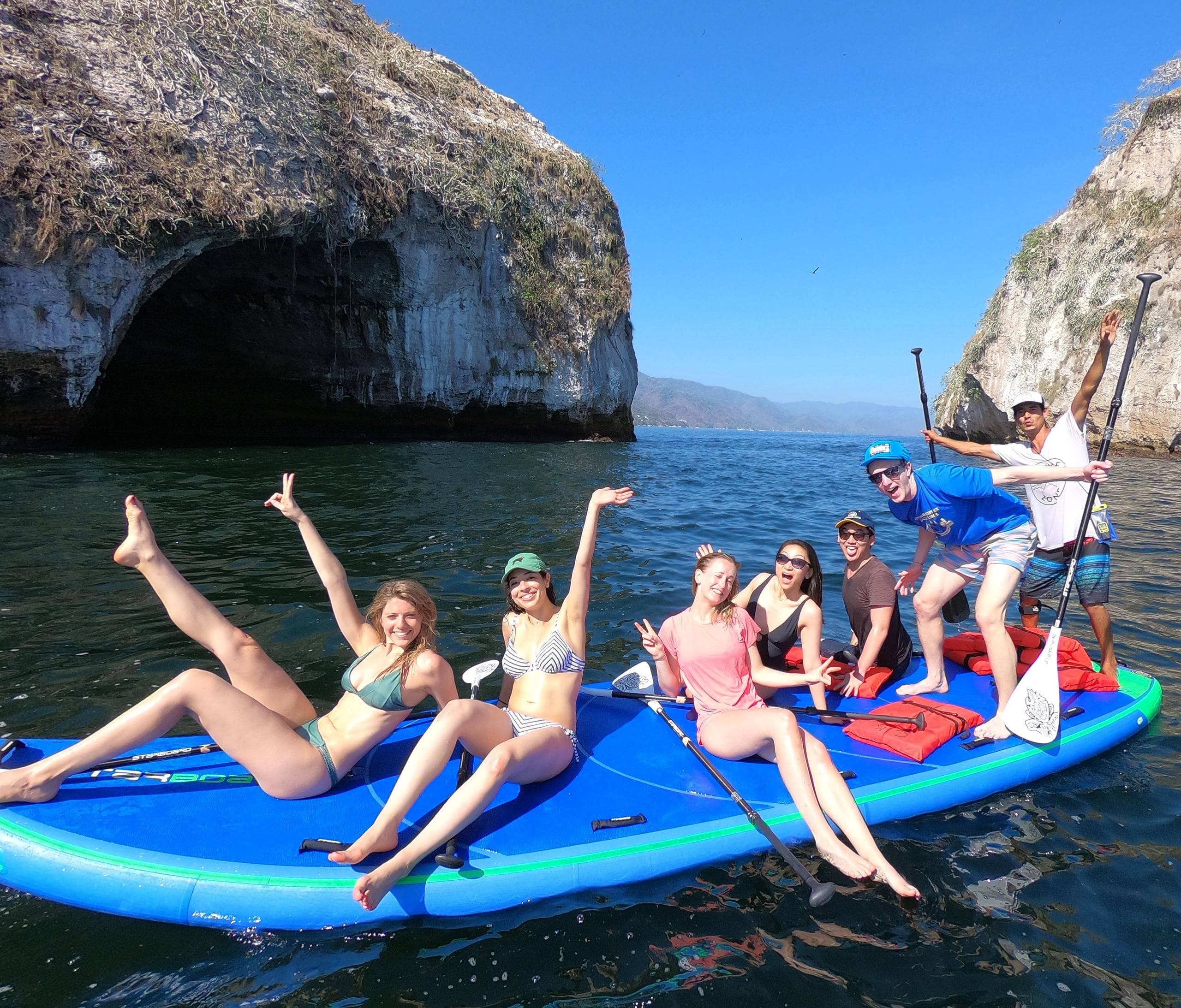 Group paddleboarding near sea caves and cliffs on sunny day