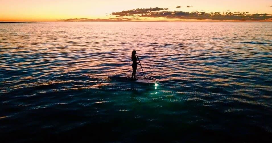 Paddleboarder at sunset in open ocean with glowing board