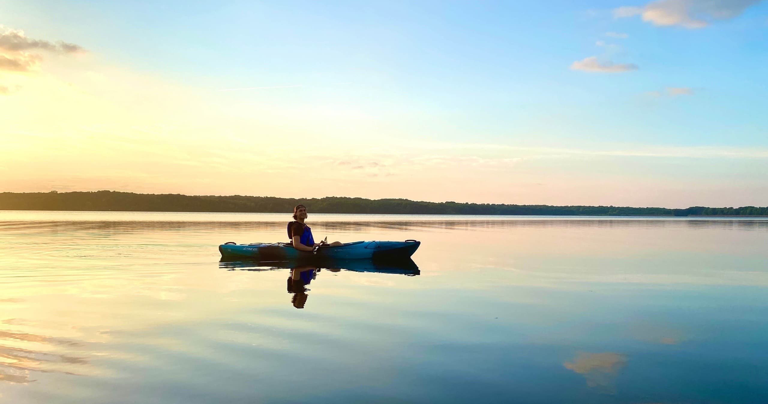 Solo kayaker silhouetted at sunset on a calm scenic lake