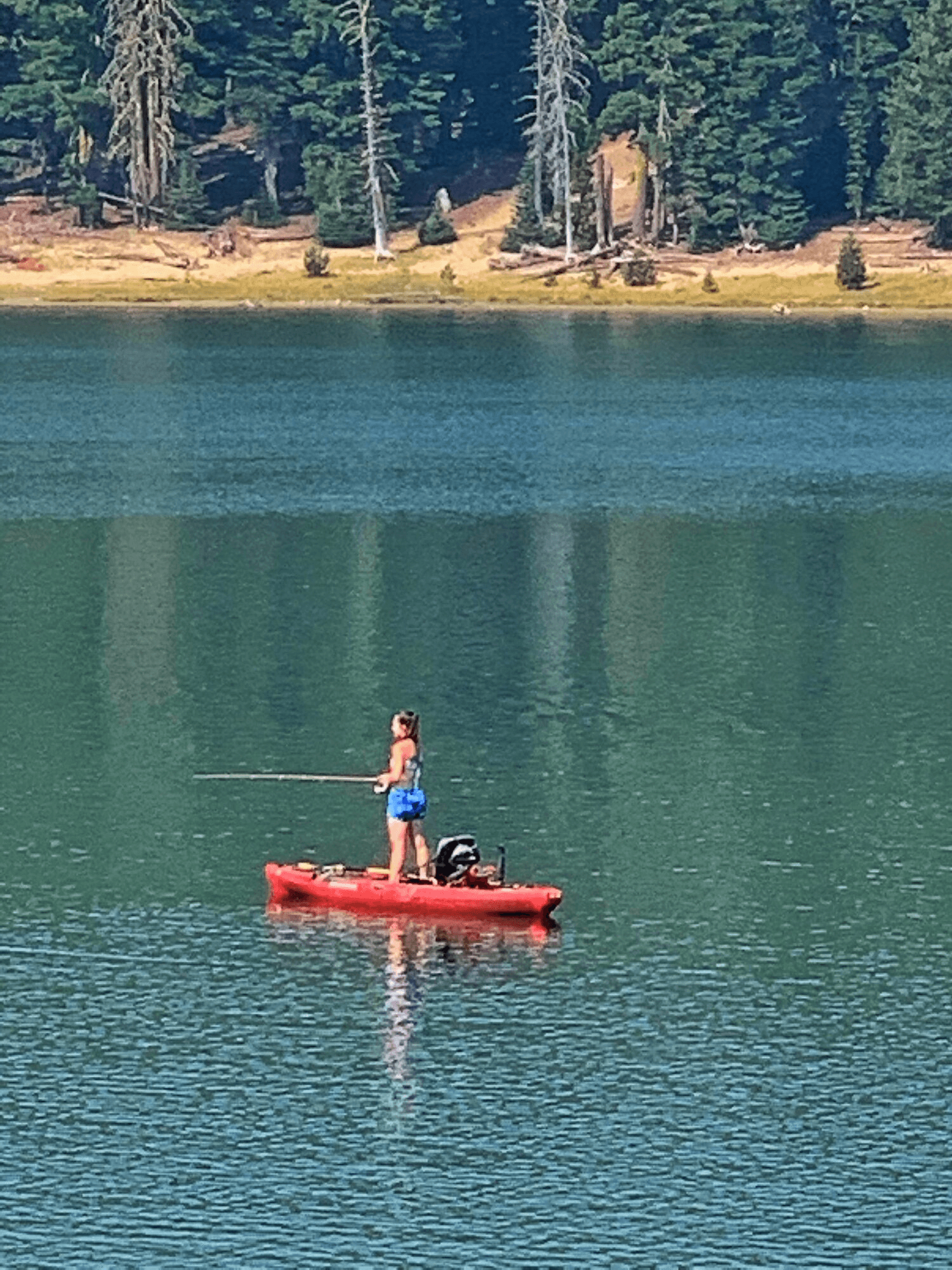 Solo angler standing on kayak in alpine lake, calm fishing