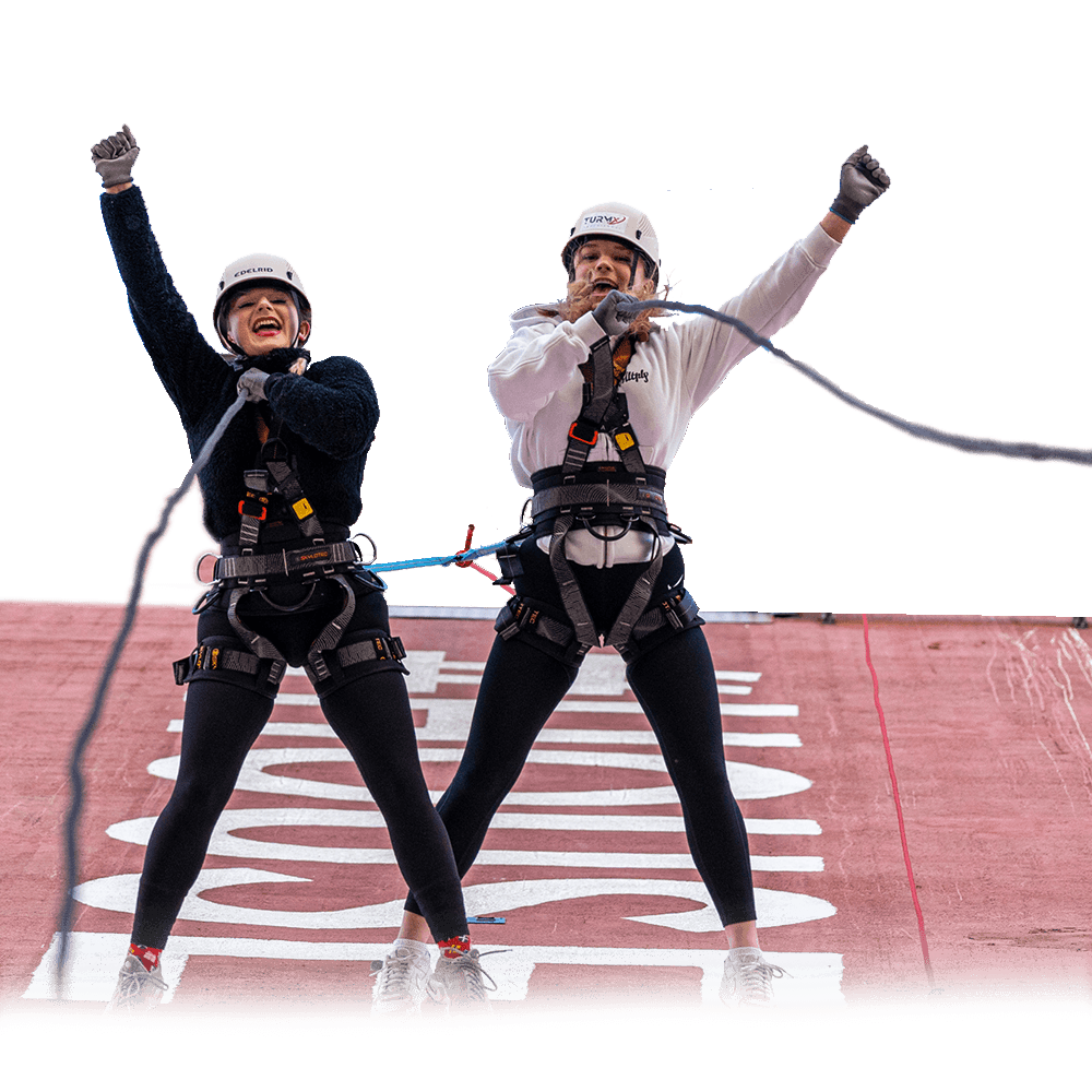 Two adventurers in harness celebrating on tower platform before zipline