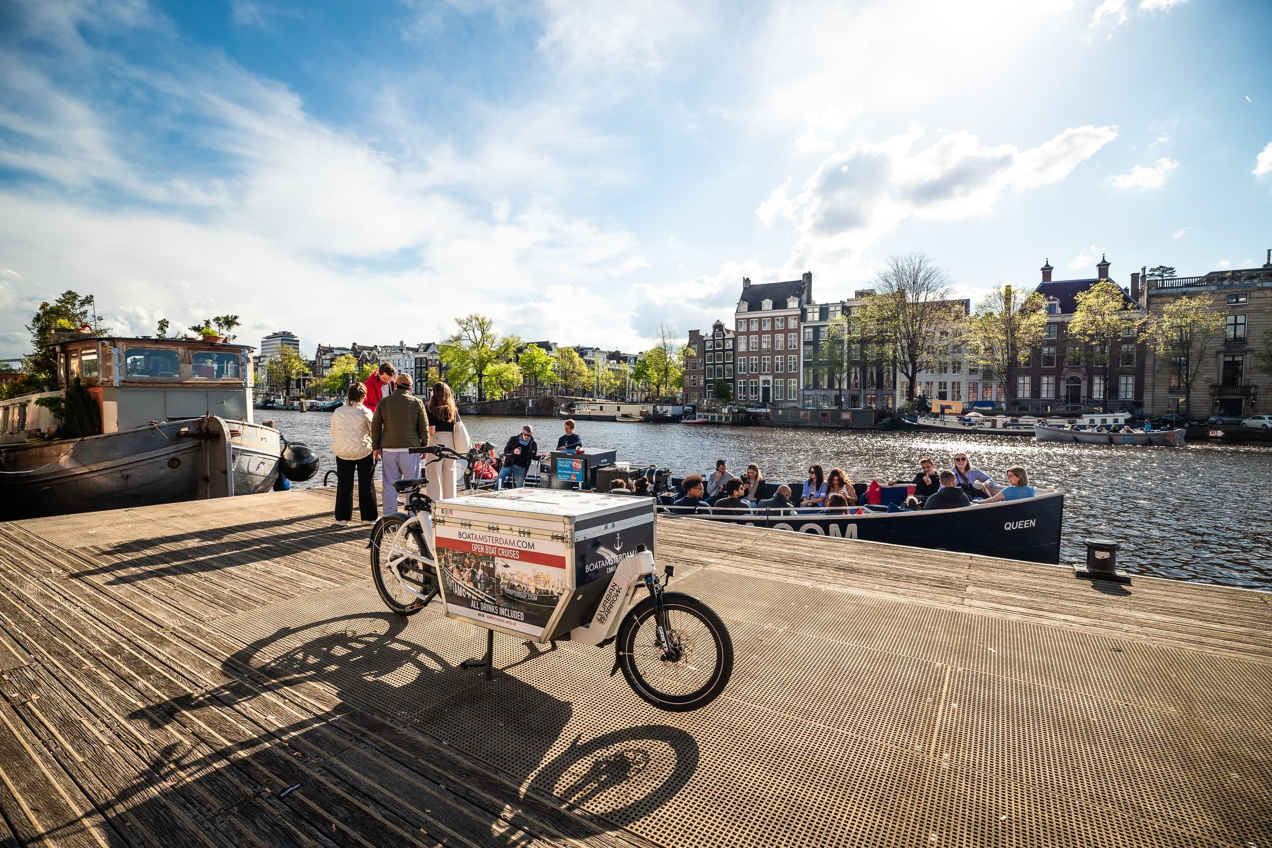 Sunny canal quay with bike and waterfront crowd in Amsterdam