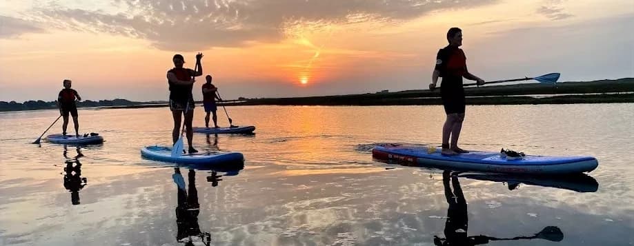 Group stand-up paddleboarding at sunset on reflective estuary