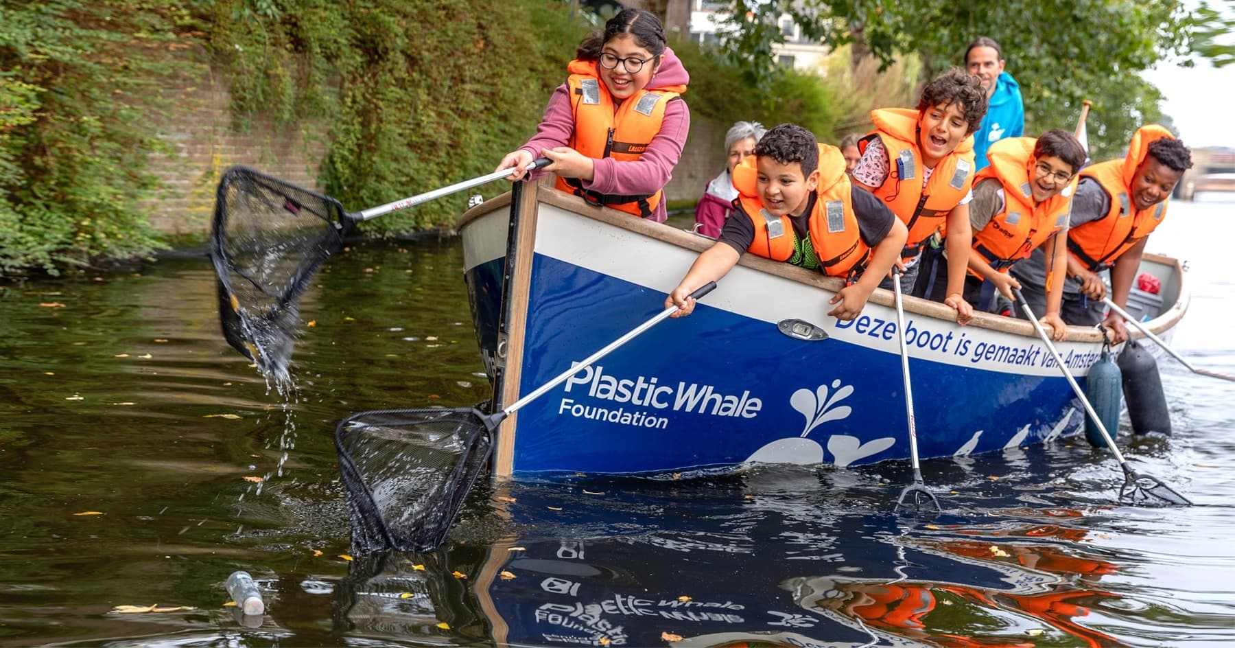 Children on PlasticWhale boat scooping litter from canal