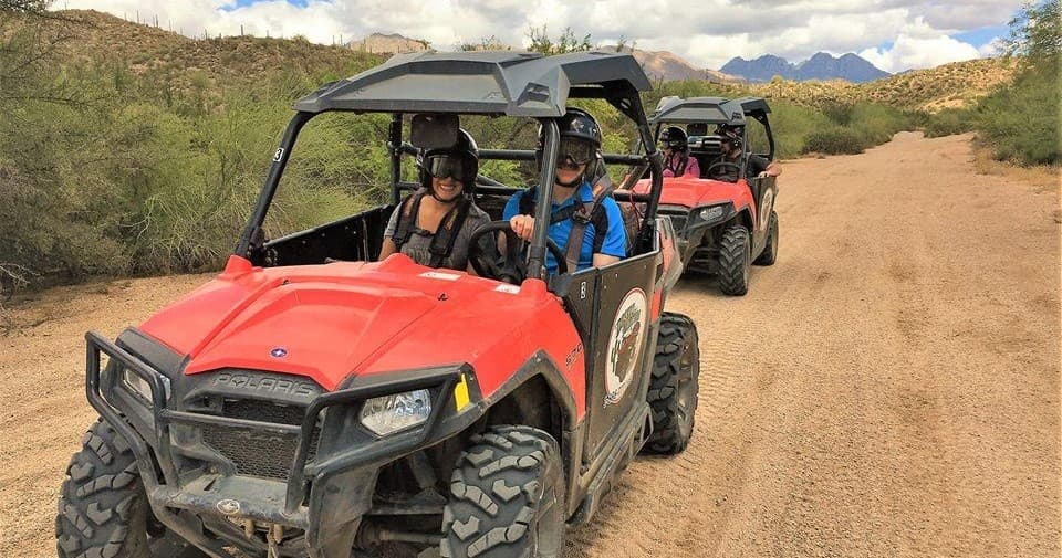 Red UTV convoy driving on desert dirt road with mountains