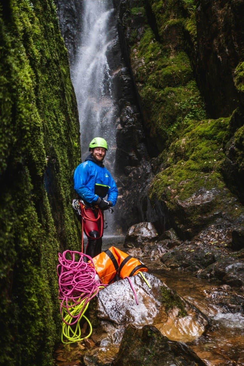 Ghyll scrambling guide beside mossy waterfall in narrow gorge