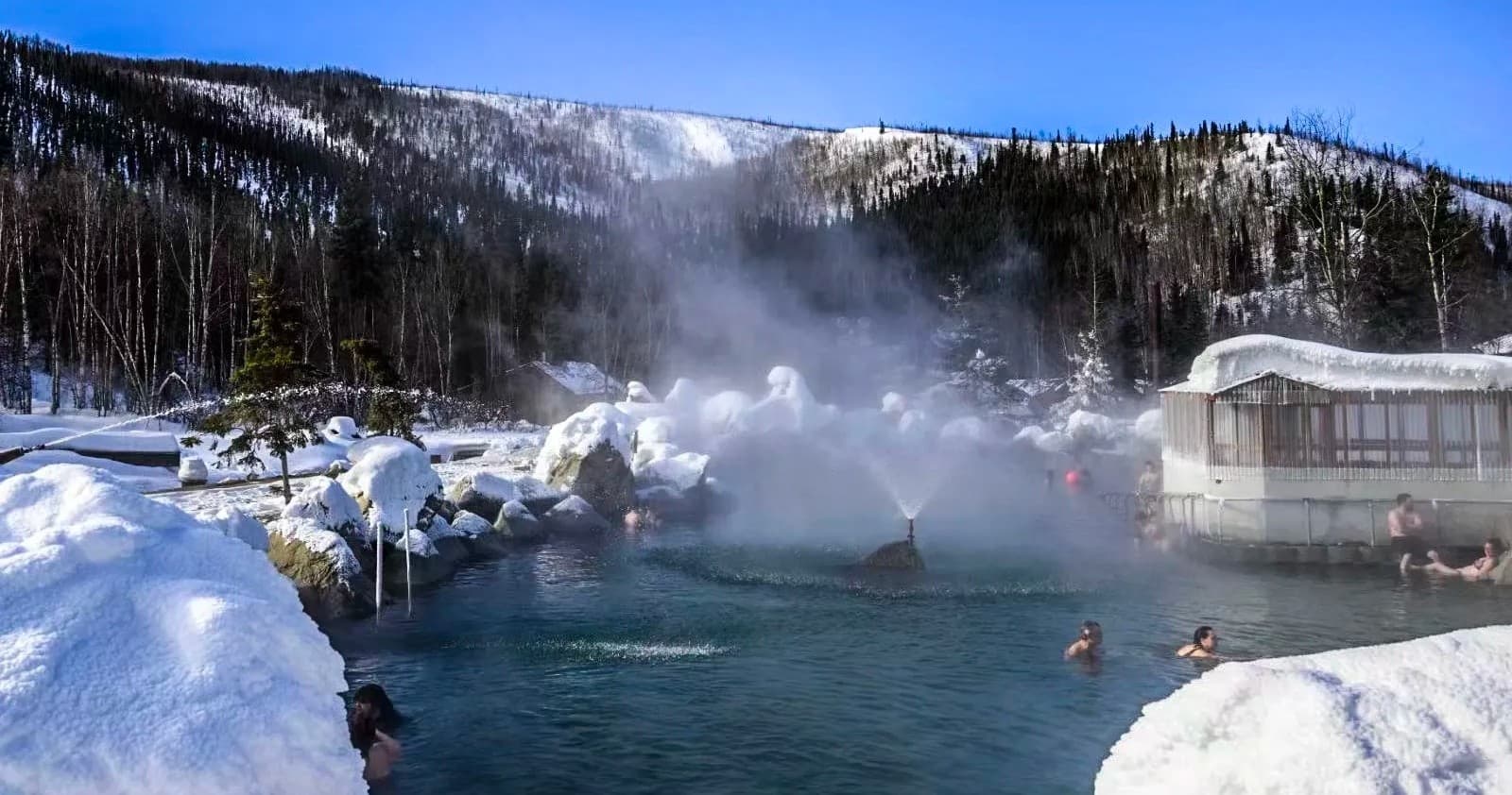 Outdoor hot springs with people bathing amid snowy Alaskan landscape