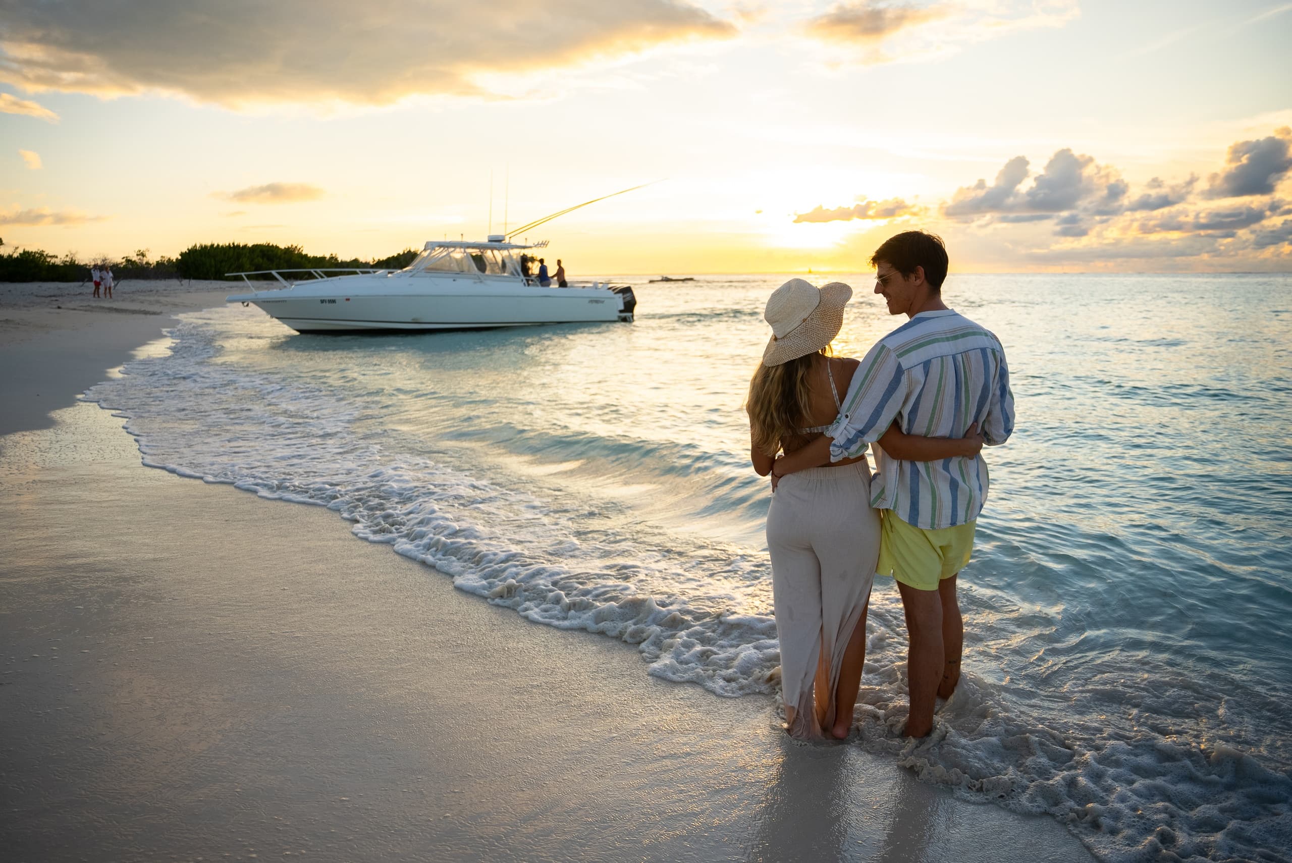 Couple strolling on tropical beach at sunset with yacht