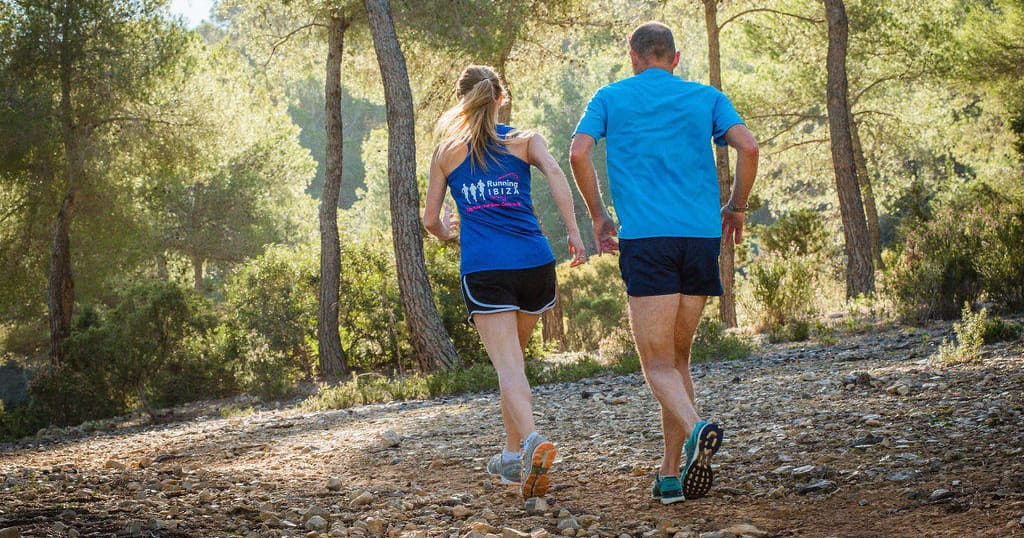 Couple trail running through shaded pine forest paths in Ibiza