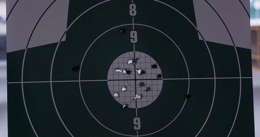 Bullet-riddled shooting target at indoor range showing tight group