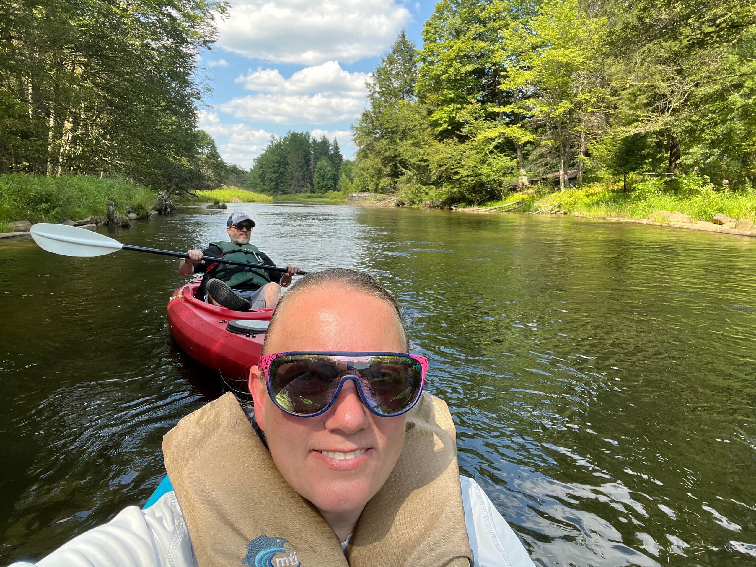 Two kayakers paddling near dock on sunny forest lake