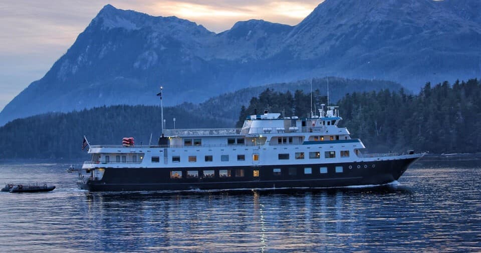 Small expedition cruise ship anchored in fjord with mountains