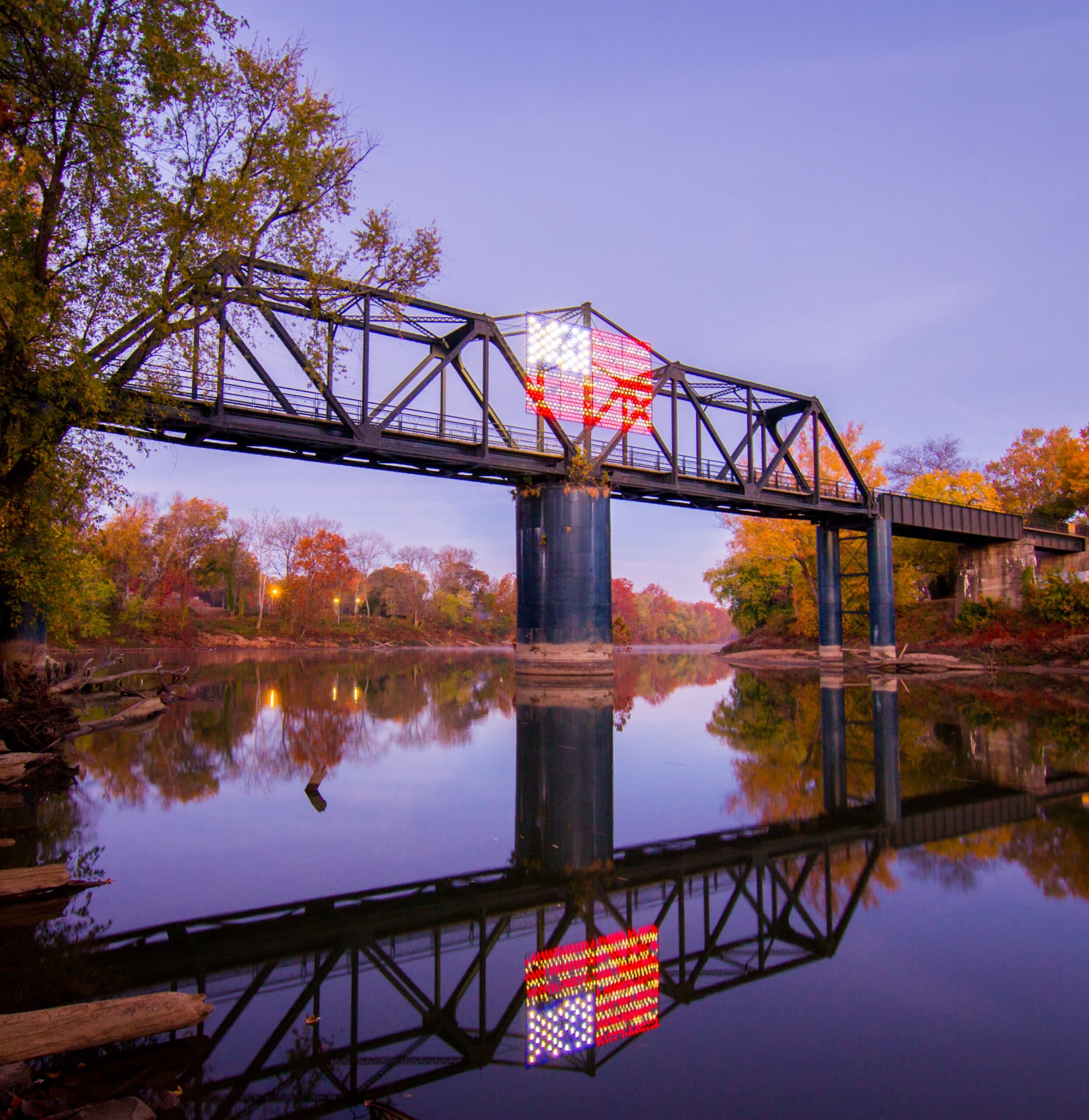 Historic truss bridge reflecting over autumn river at sunset