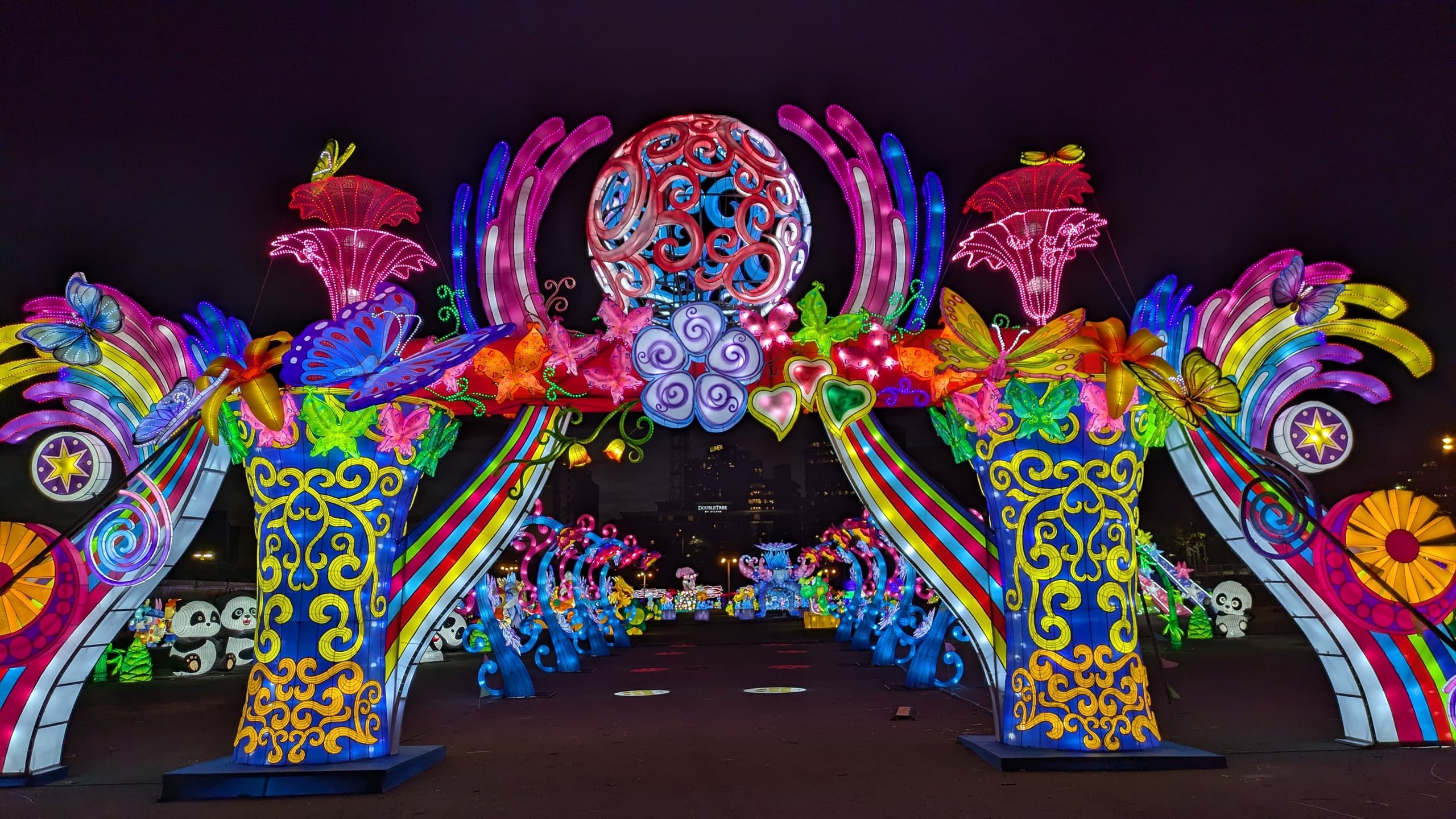 Visitors walking under colorful illuminated lantern arch at nighttime festival