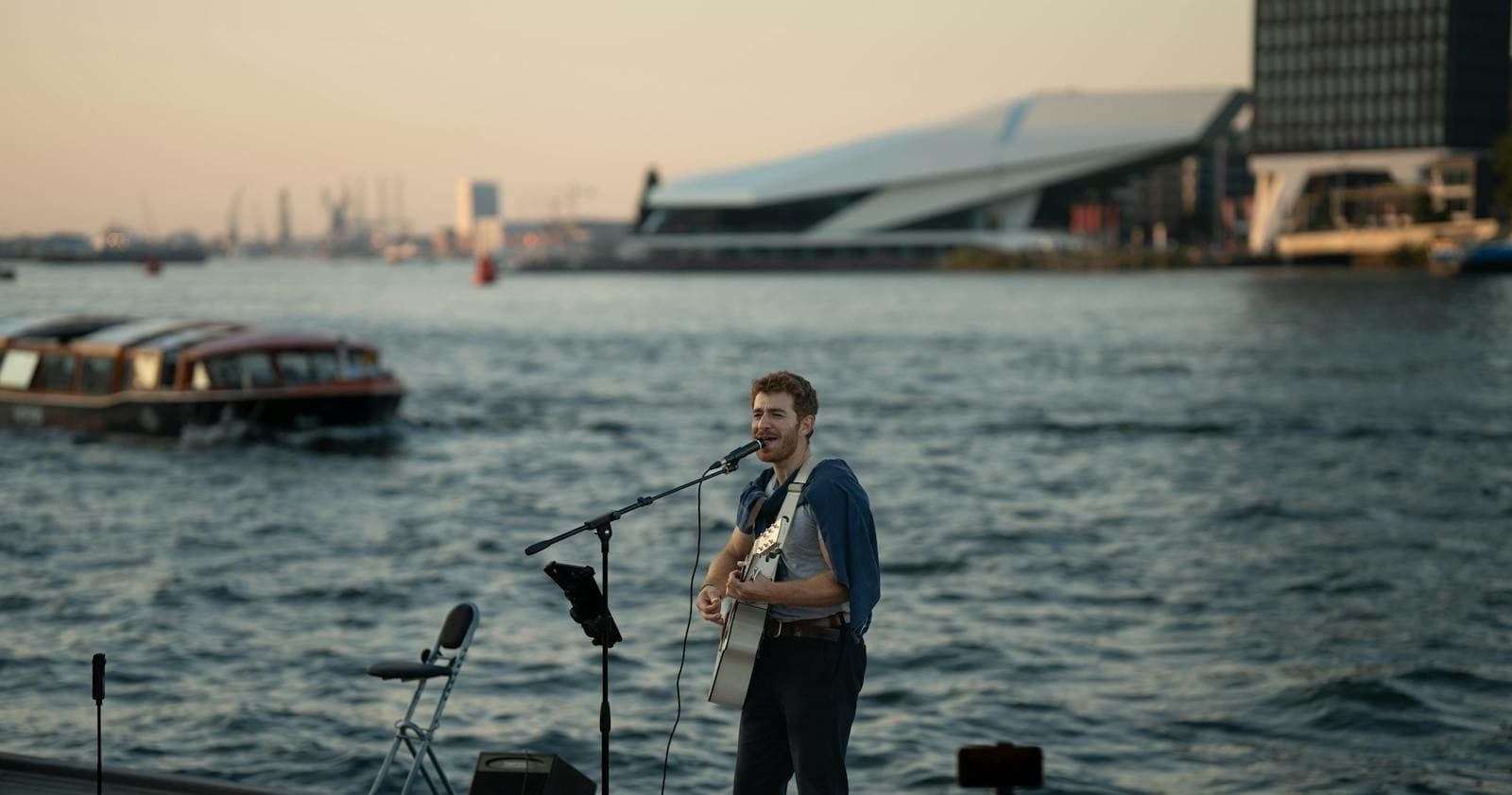 Singer performing on waterfront stage with harbor backdrop