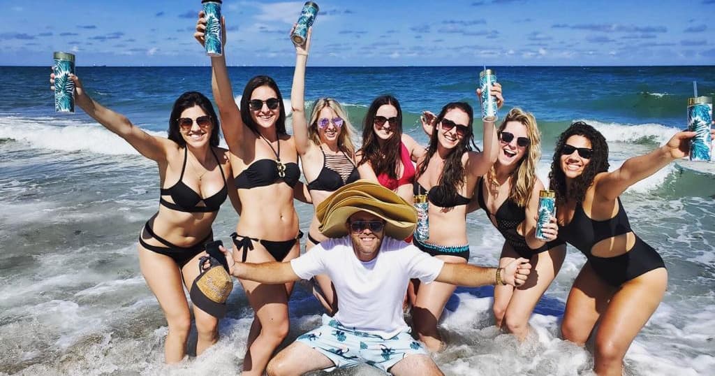 Group of women cheering in bikinis on ocean beach shore