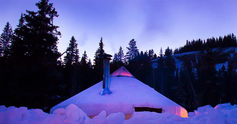Twilight yurt with chimney under purple alpine sky in snowy trees