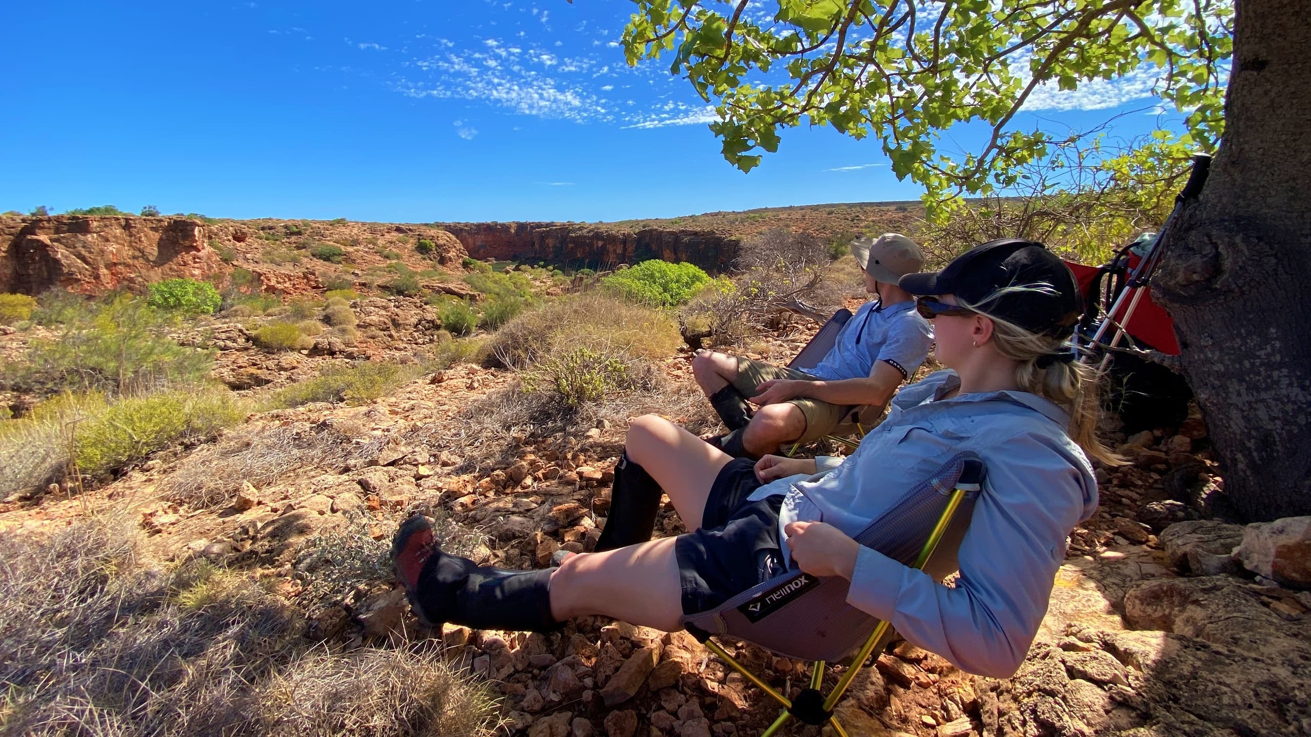 Hikers resting under a tree on rocky scrubland during trek