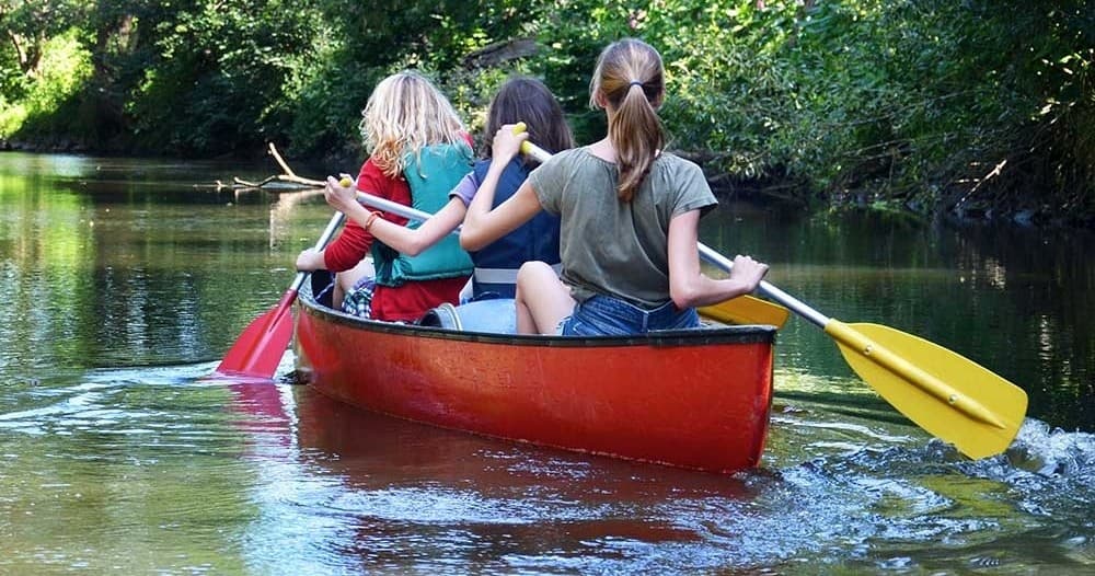 Family canoeing on shaded winding creek, kids paddling together
