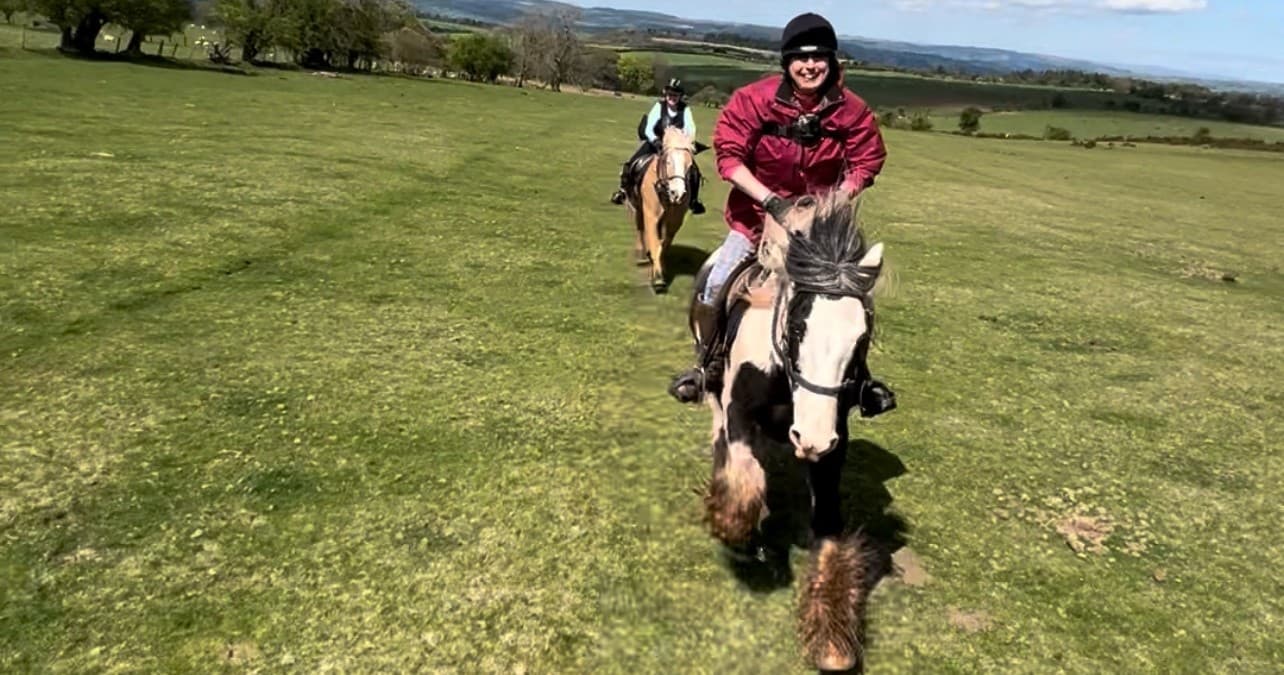 Riders galloping across open grassy fields on a trail ride