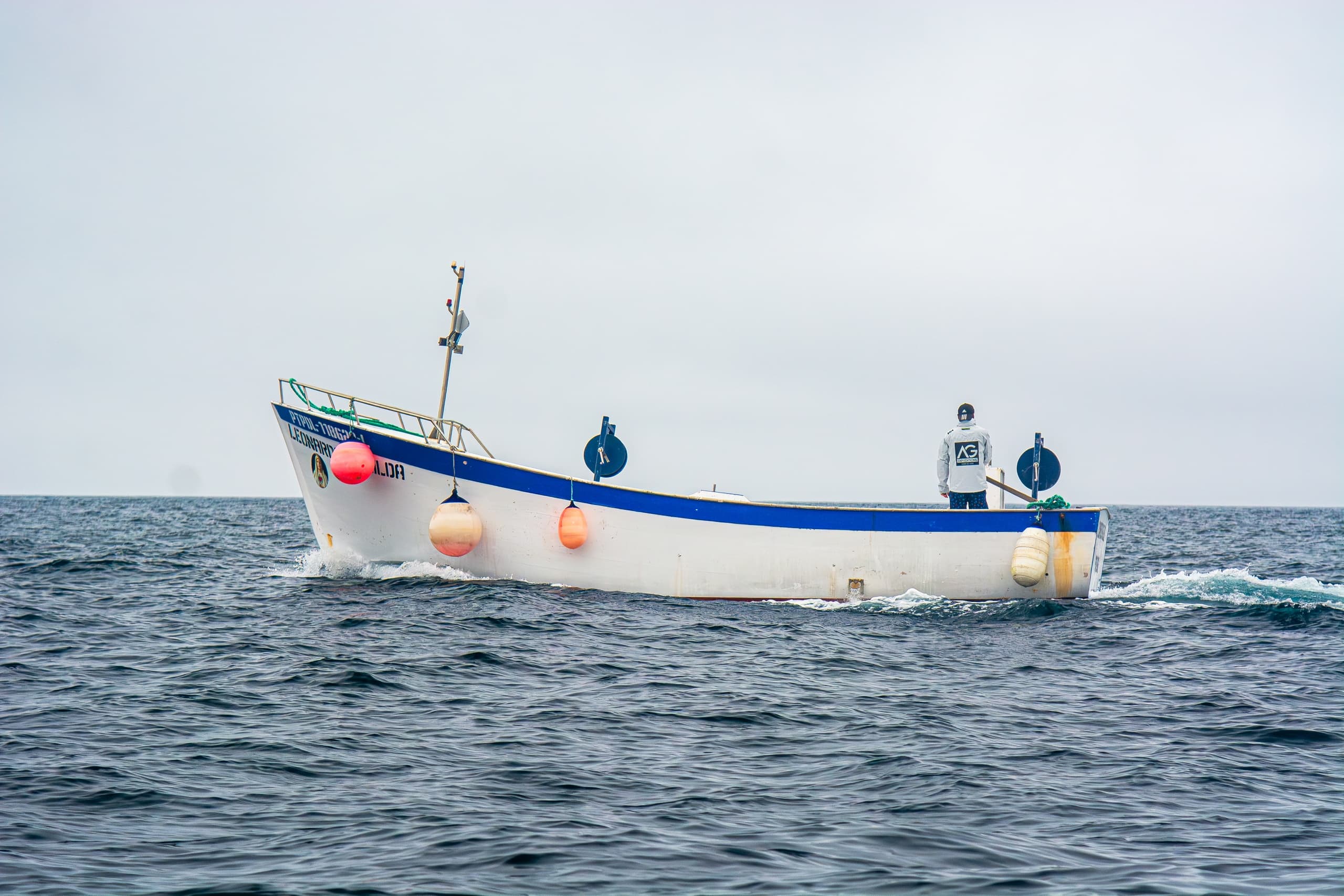 Small fishing boat on calm sea under overcast sky near coast