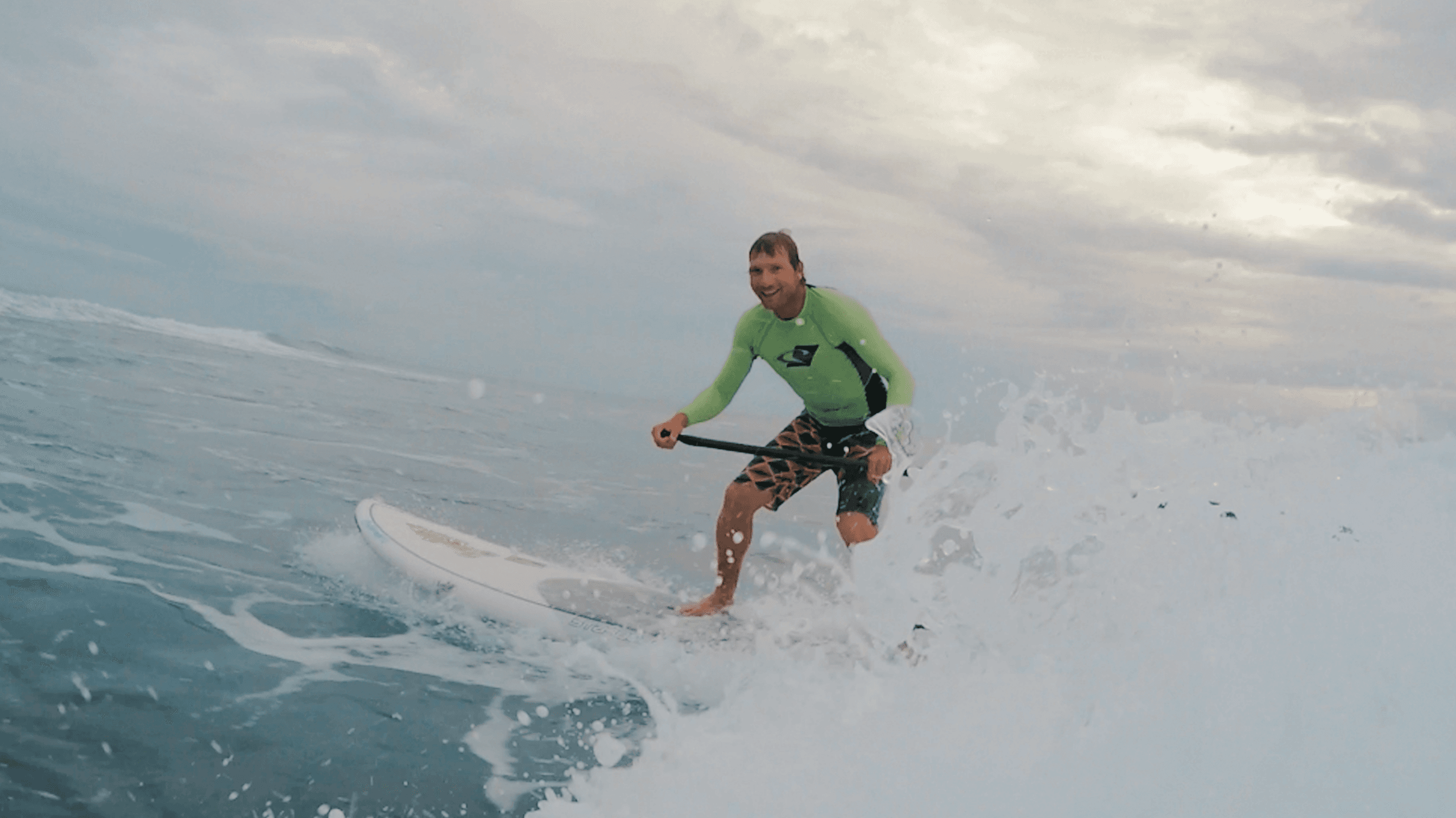 Surfer in green rash guard trimming high on an open wave