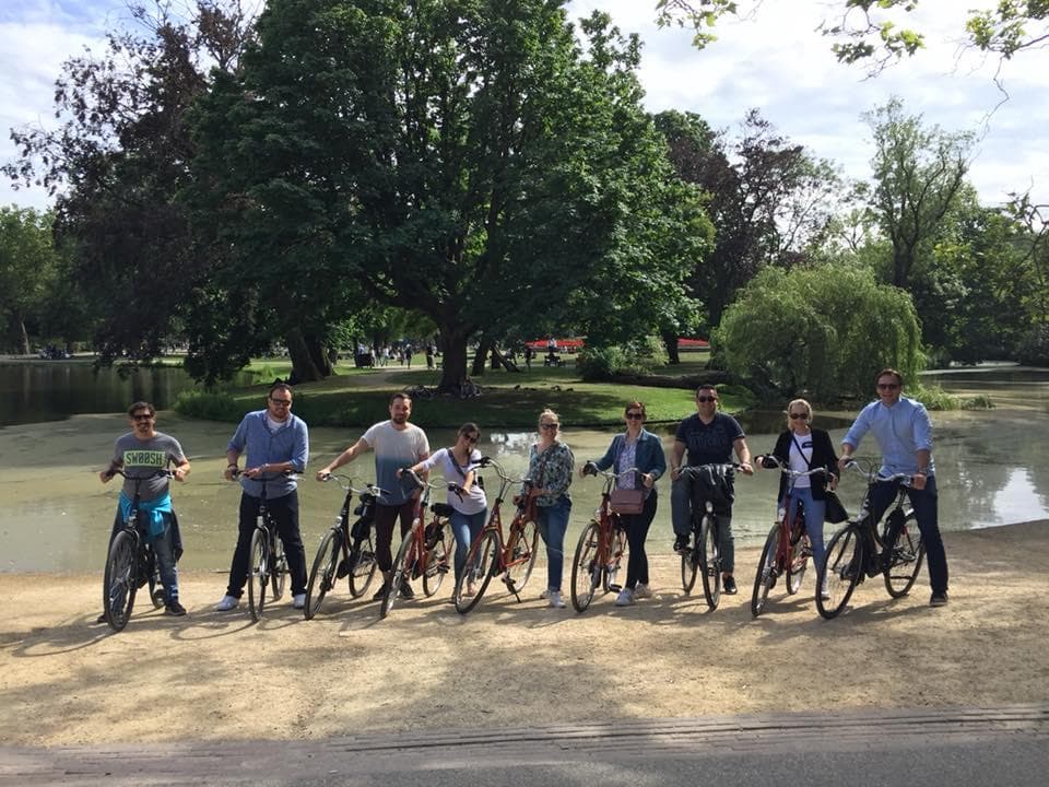 Group cycling along a calm pond in a scenic park, Amsterdam bike tour