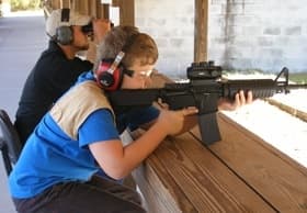 Youth aiming rifle on outdoor shooting bench at range