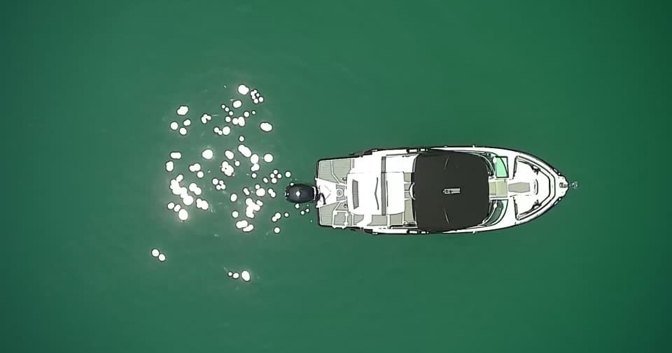 Aerial top-down view of boat on emerald sea with sun glints