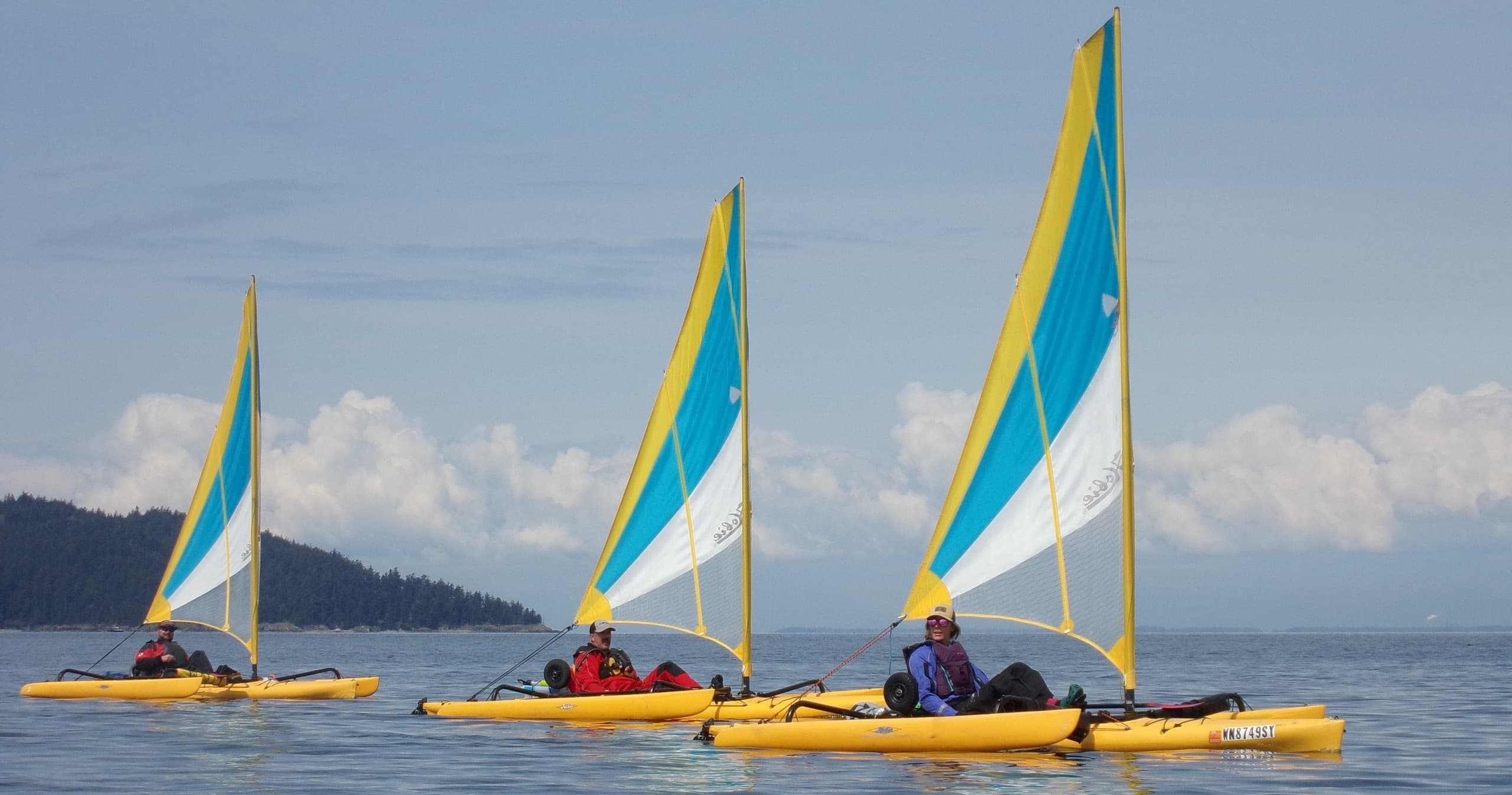 Sail-equipped kayakers paddling calm coastal waters near islands