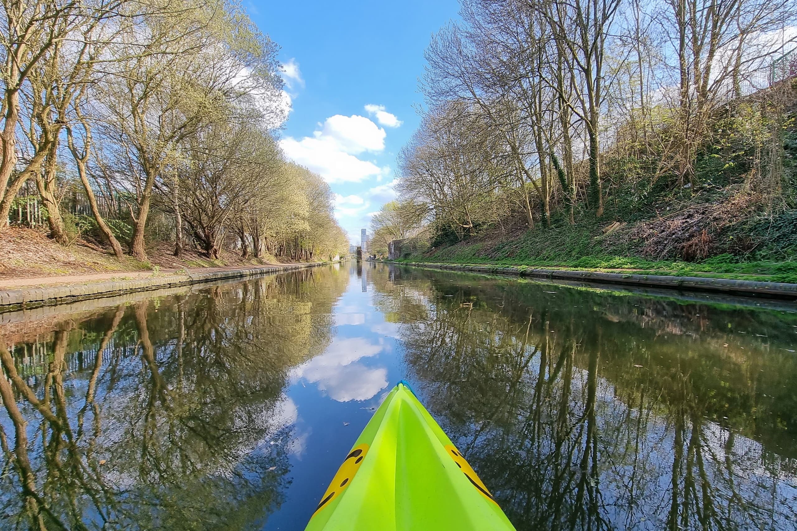 Kayak paddling along reflective tree-lined canal in spring