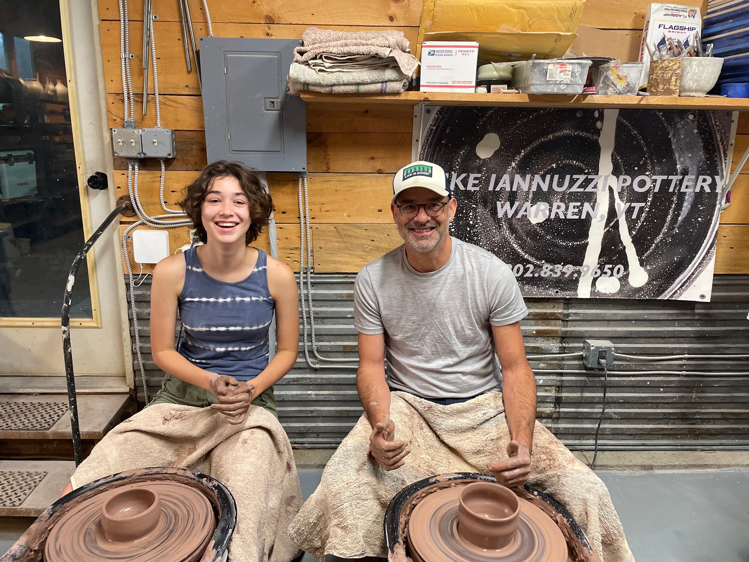 Two potters shaping clay on wheels in indoor pottery studio
