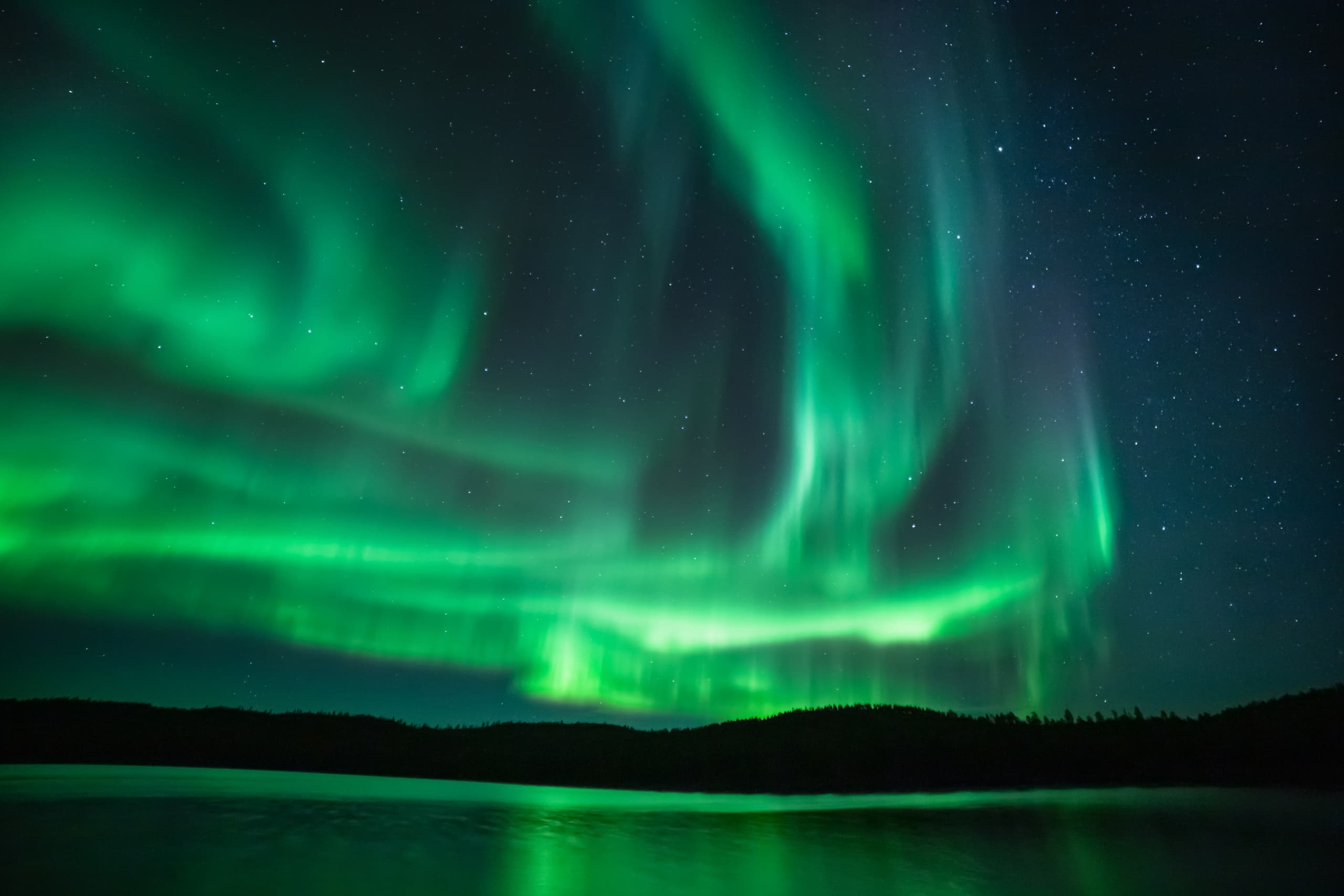 Vivid northern lights over dark lake in Lapland night sky