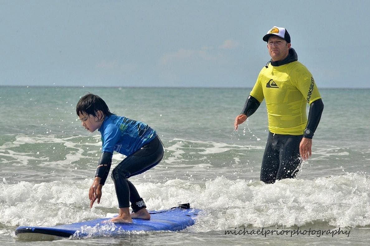 Child learning to surf with instructor in calm Whangamata surf