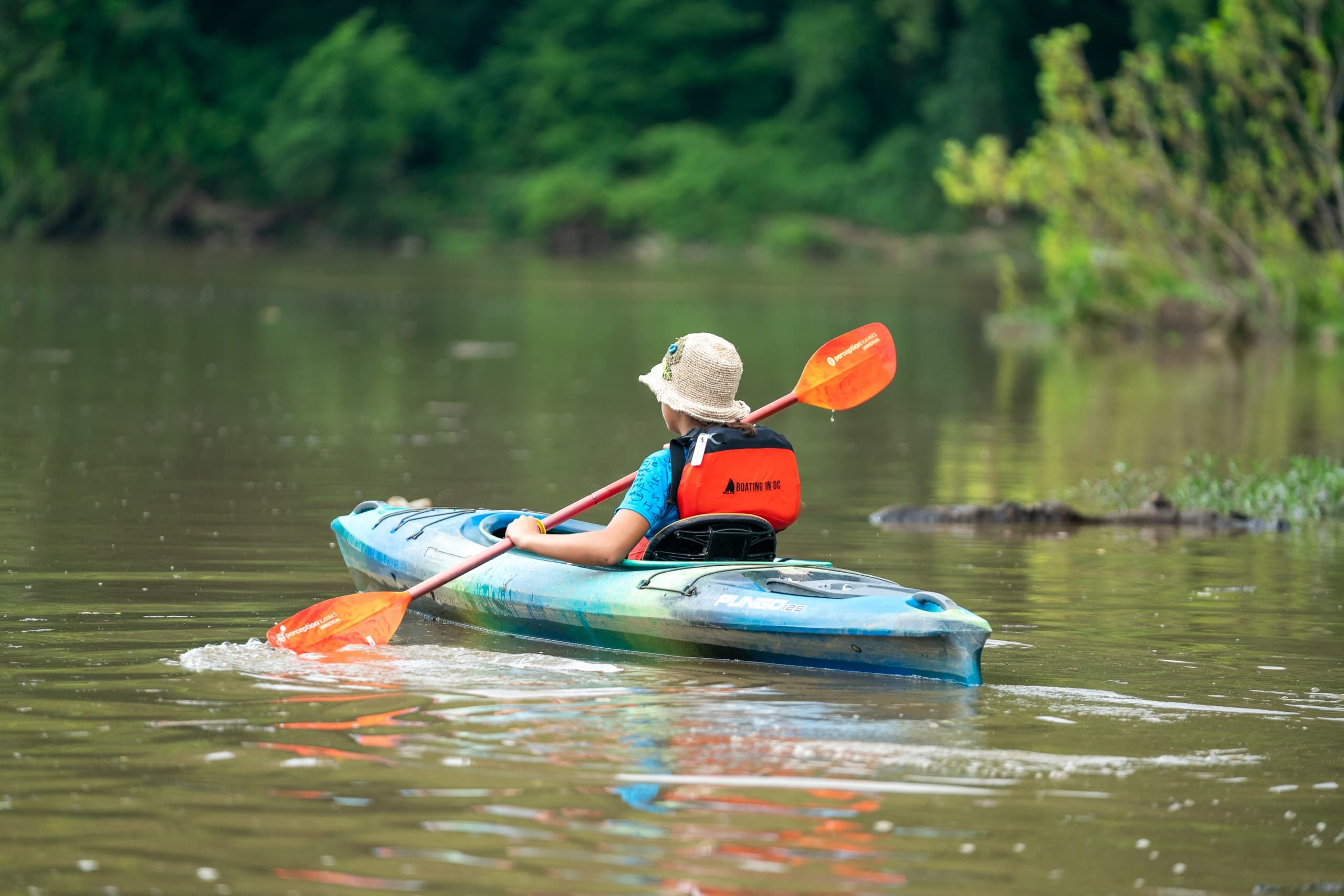 Solo kayaker paddling on calm river near wooded shoreline