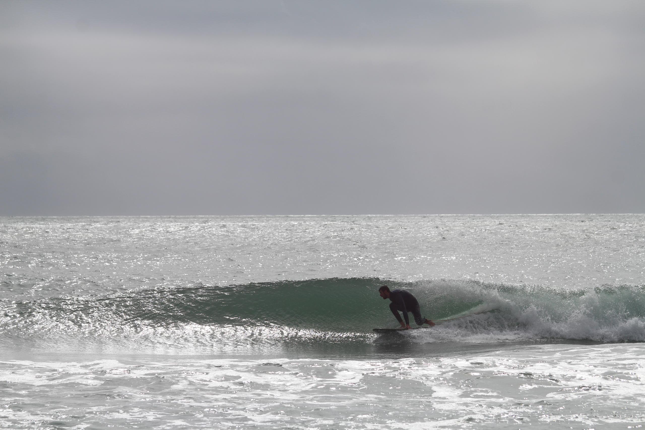 Surfer riding a clean right-hand wave near sandy shoreline