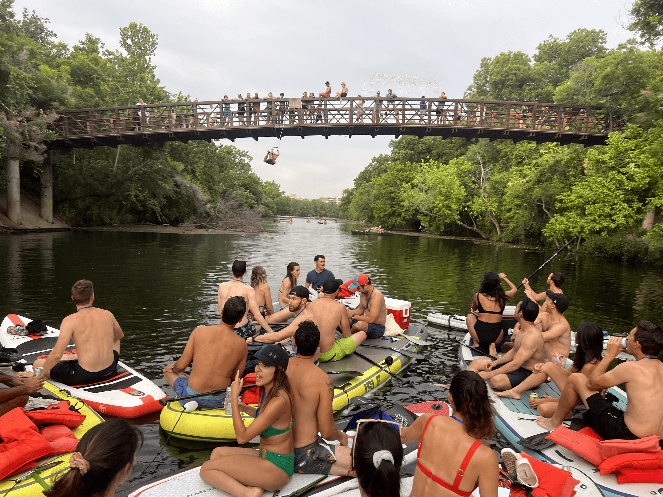 Group of tubers and kayakers crowded under pedestrian bridge on river