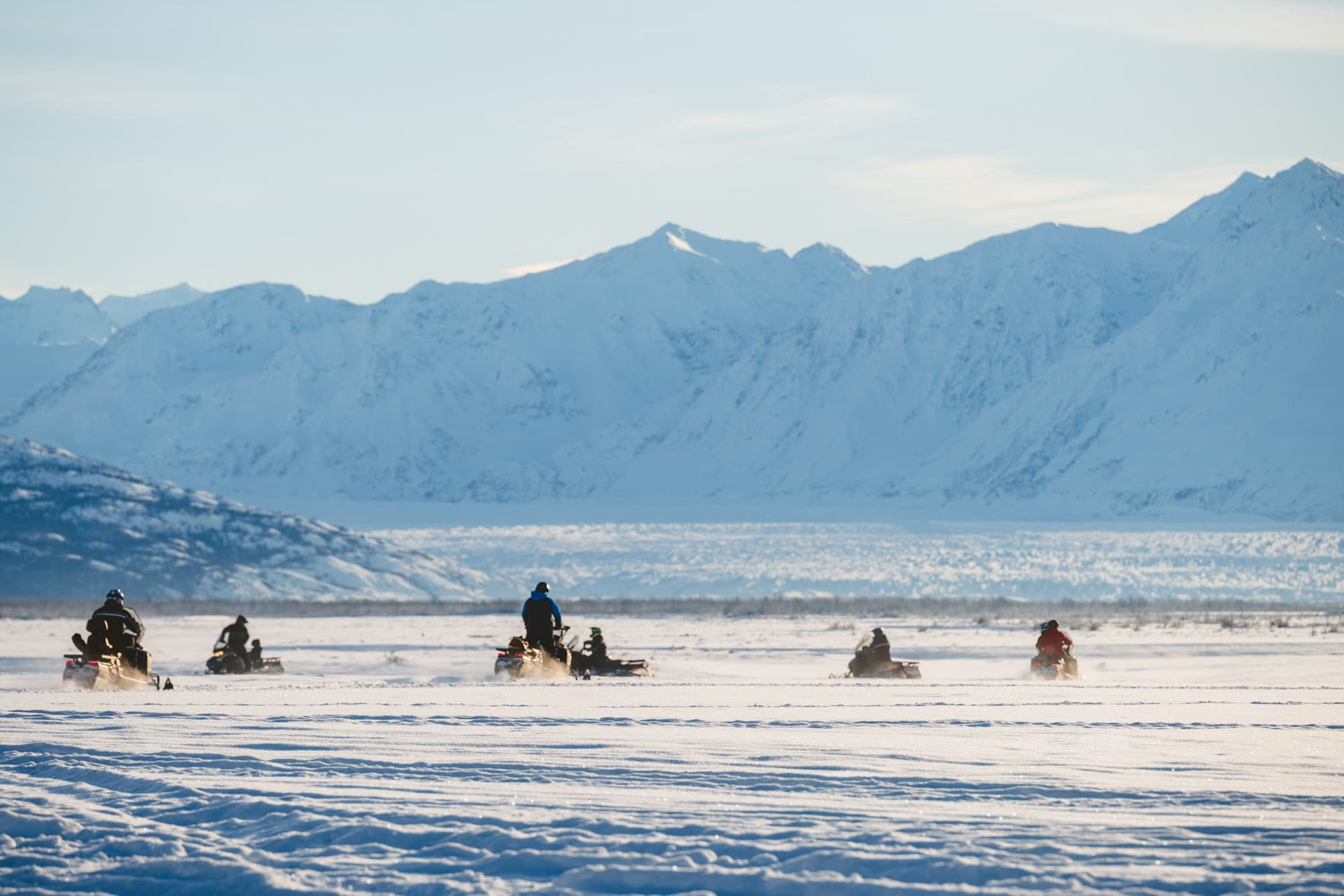 Snowmobile expedition crossing frozen plain toward mountains