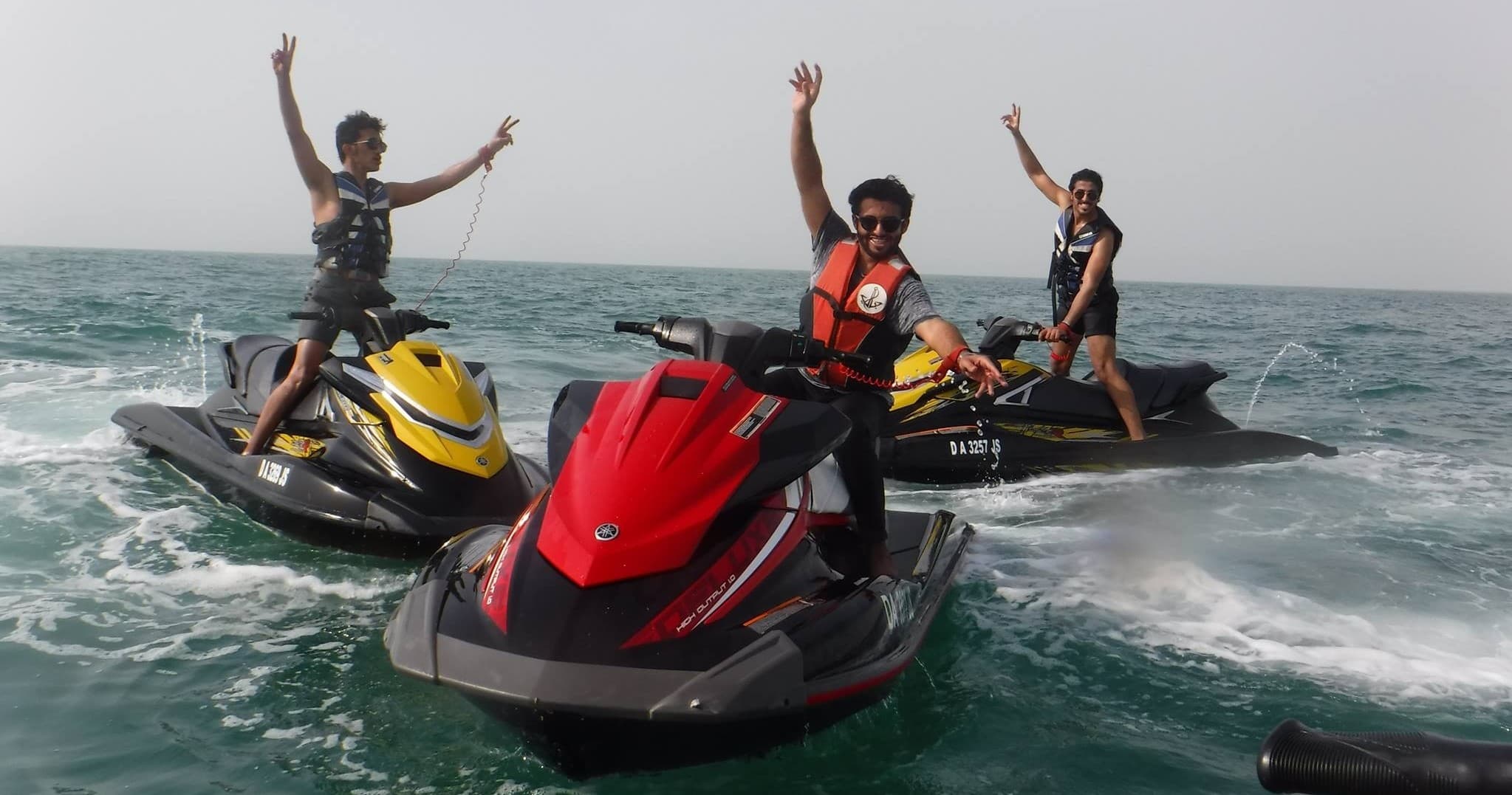 Friends on jet skis cheering offshore Dubai, high-energy water adventure