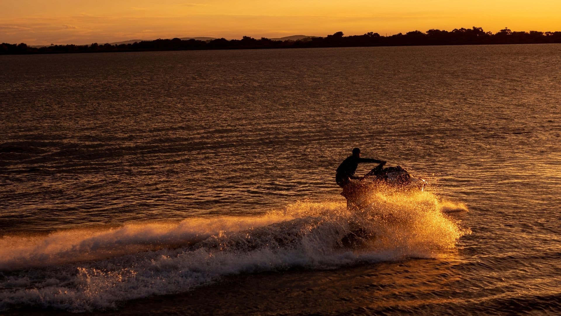 Rider on jet ski cutting waves at sunset on open water