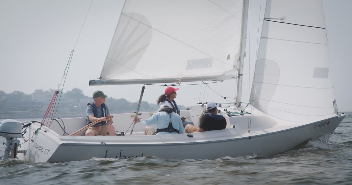Leisure sail with four crew aboard a white sloop on water
