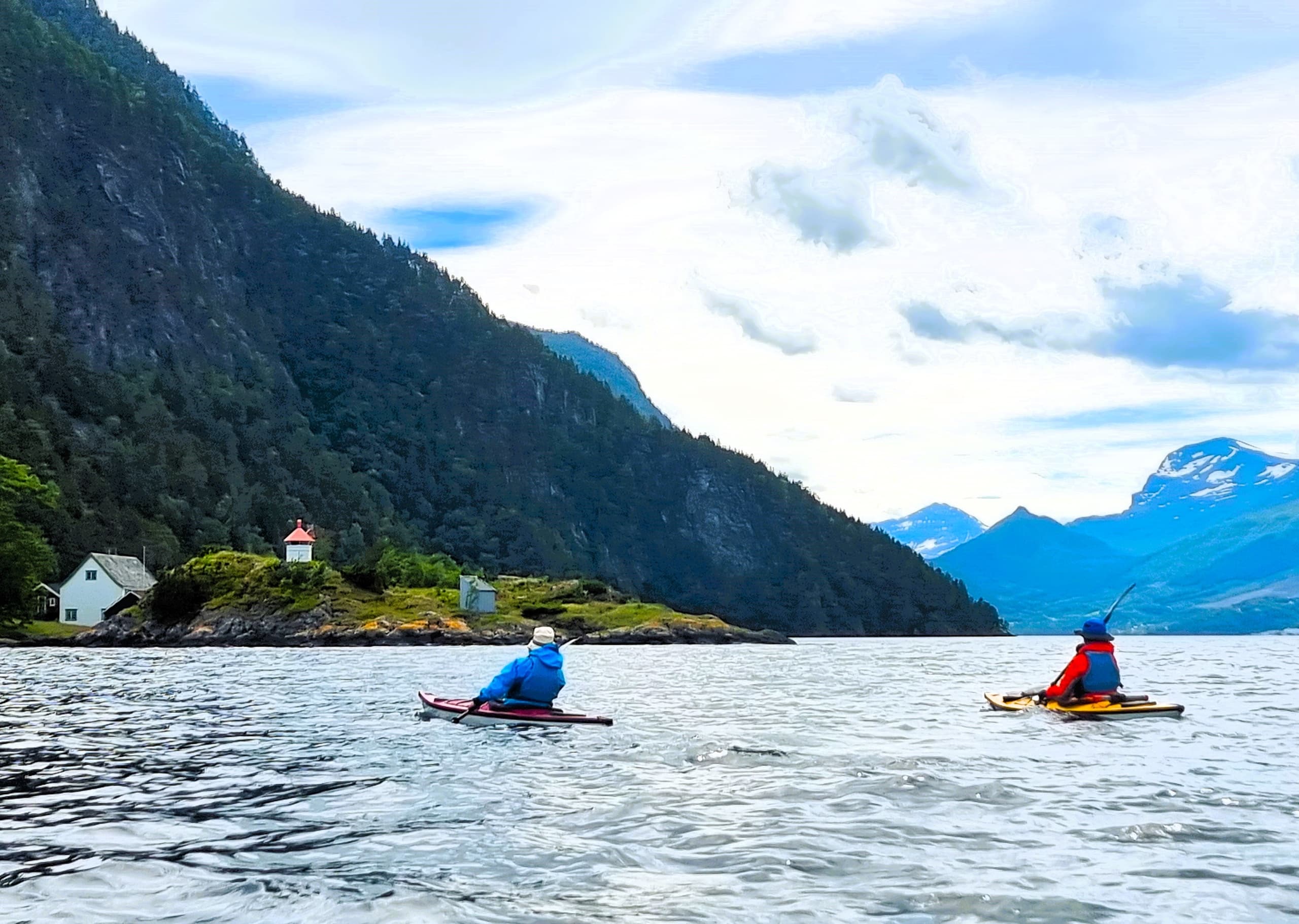 Two kayakers paddling across glacial fjord with mountains
