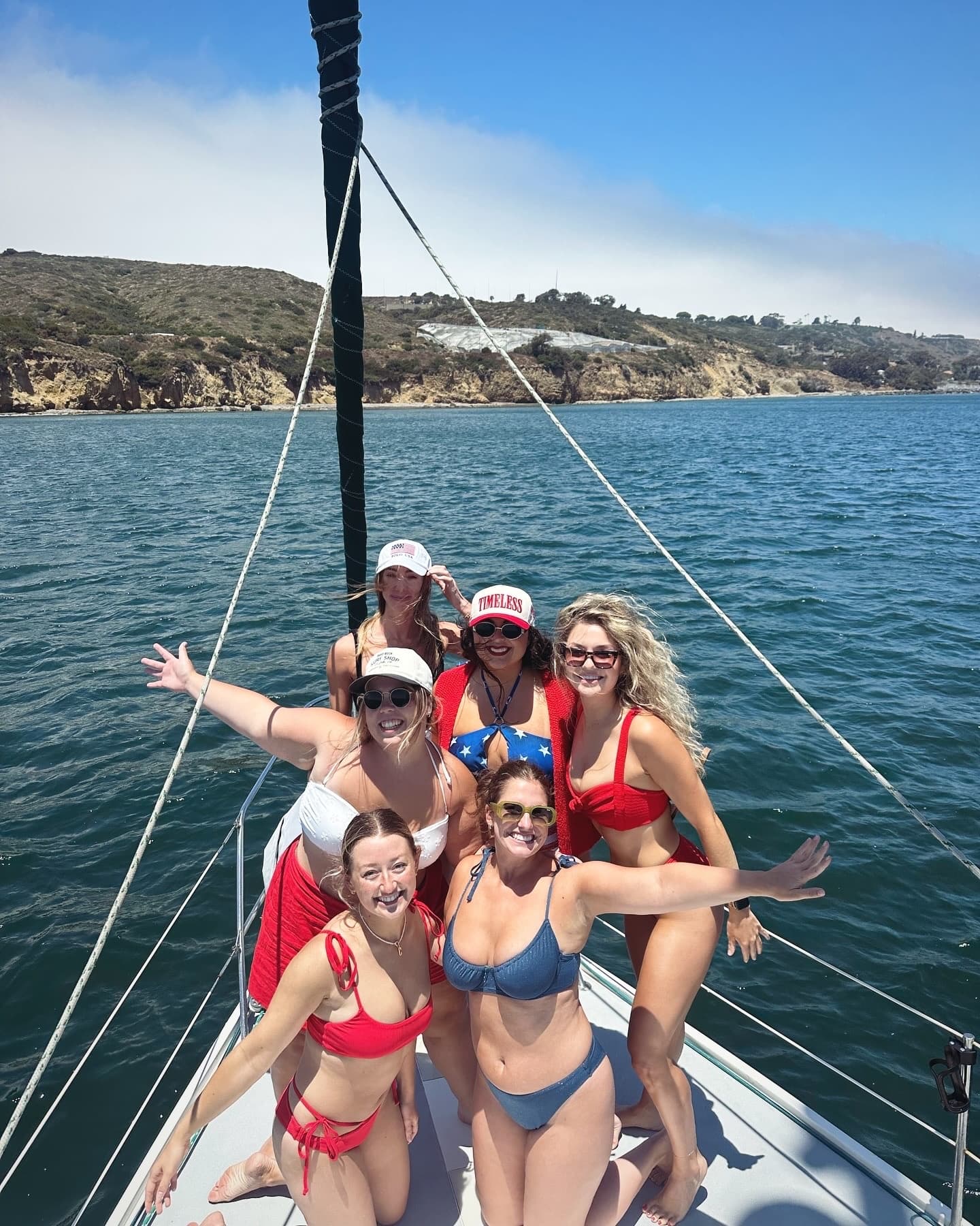 Group enjoying sailing and sun on bow of sailboat near cliffs